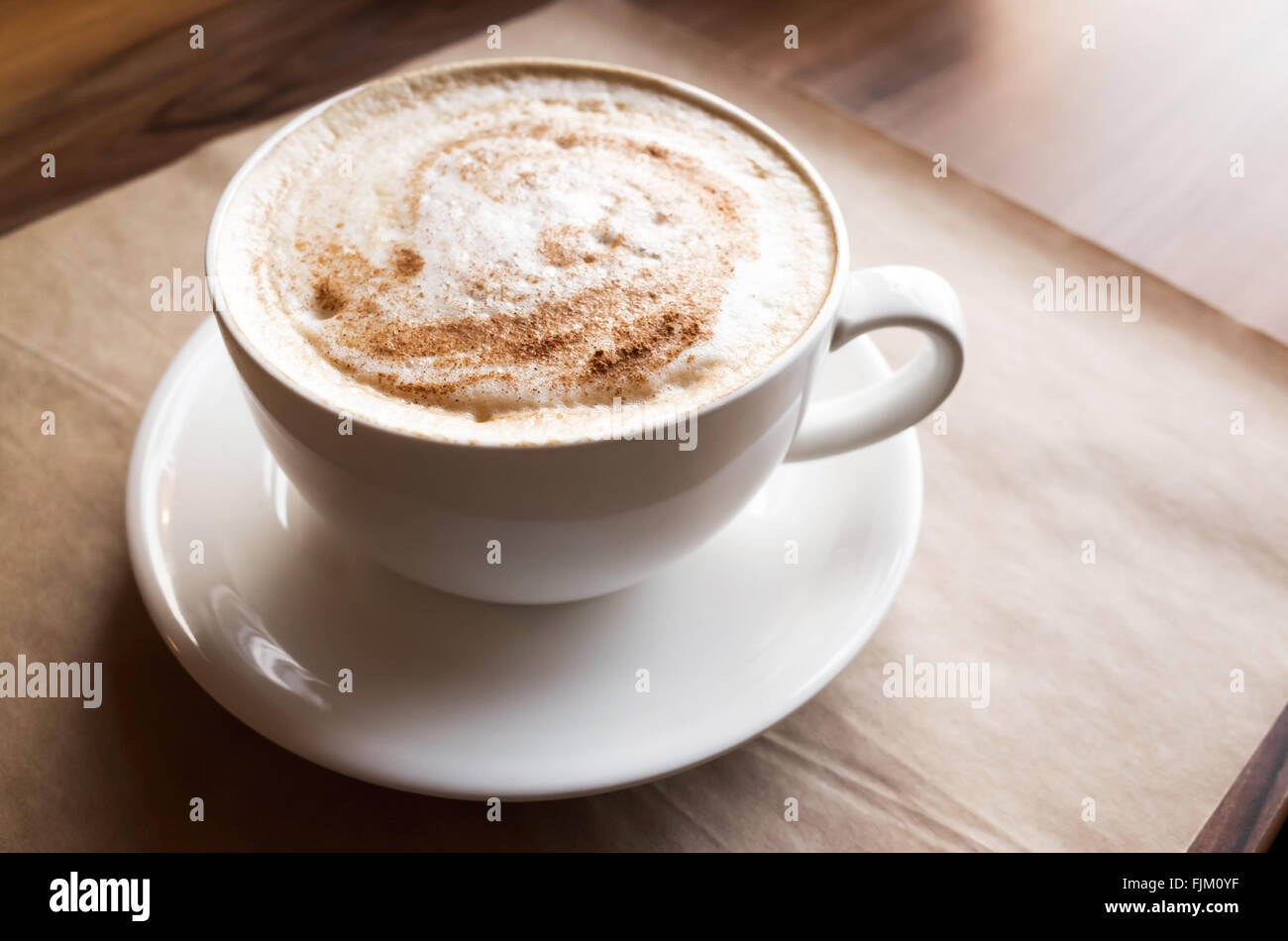 Cappuccino. Tasse Kaffee mit Milchschaum steht über Altpapier auf Holztisch in cafeteria Stockfoto