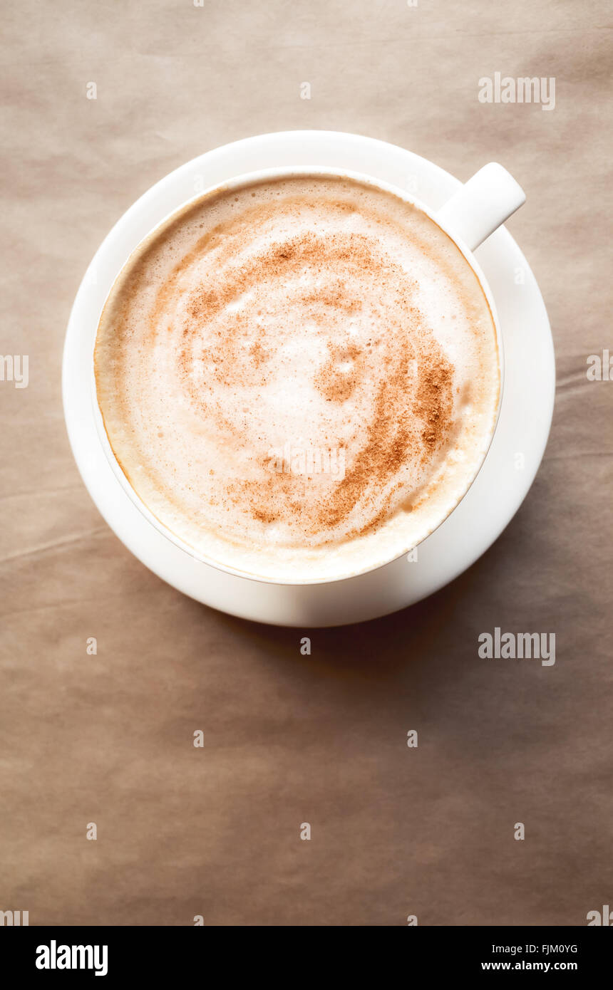 Cappuccino. Tasse Kaffee mit Milchschaum steht über Altpapier auf Tisch in der Cafeteria. Ansicht von oben, vertikale Zusammensetzung Stockfoto