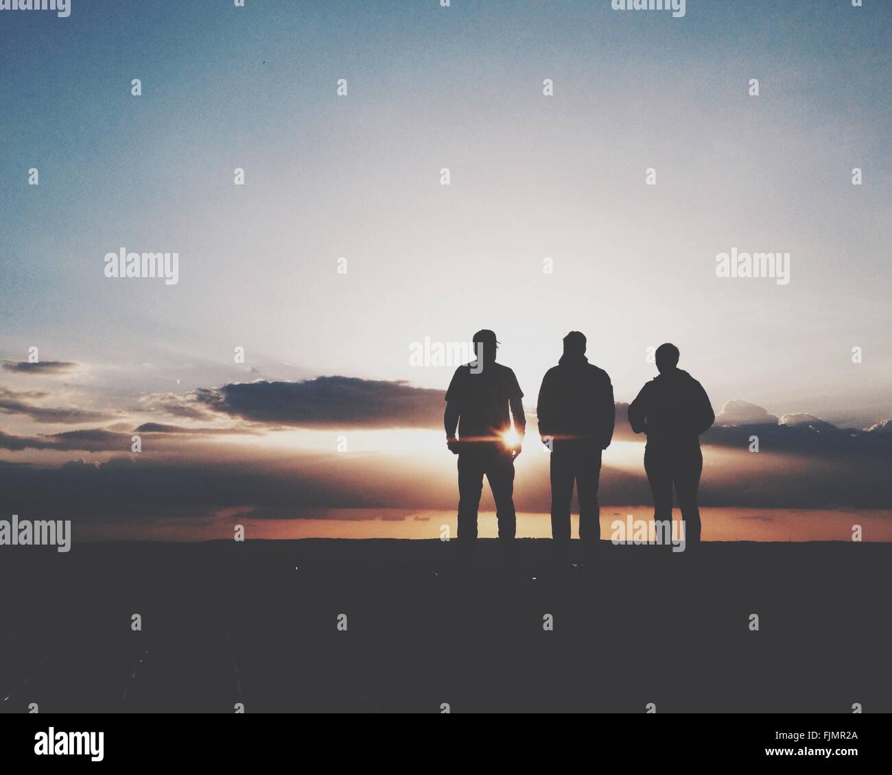 Silhouette von drei Menschen stehen bei Sonnenuntergang Stockfoto