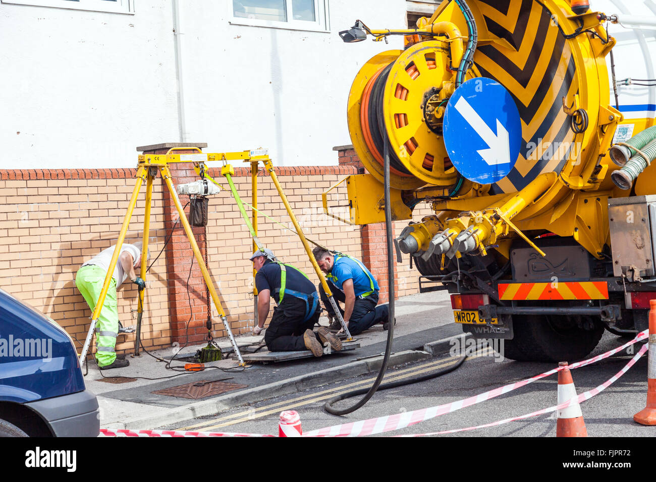 Arbeiter tragen Sicherheitsgurte, wie sie auf Kanalisation Raster auf Supermarkt-Parkplatz funktionieren. Prestatyn, Wales, Vereinigtes Königreich Stockfoto
