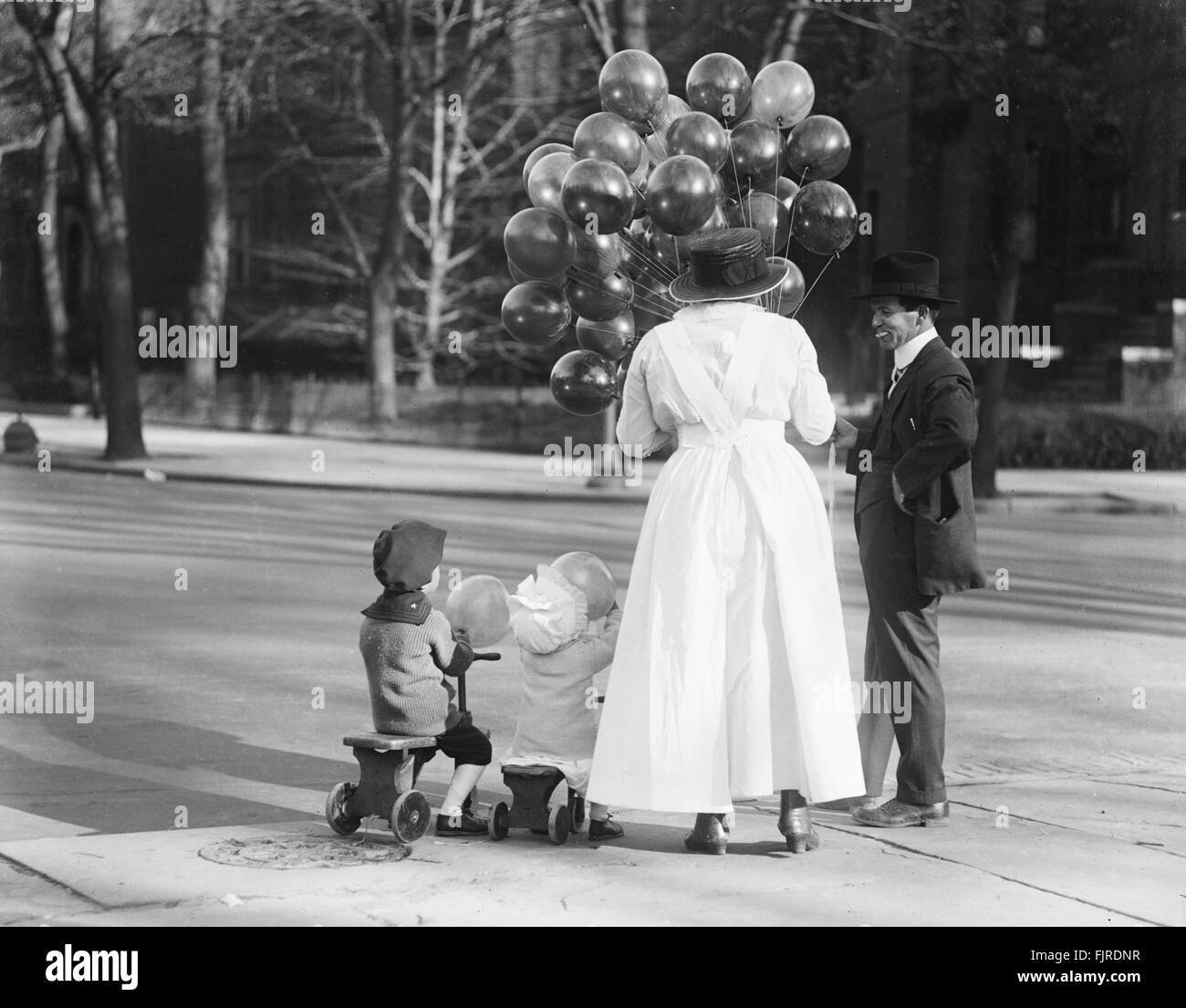 Frau mit zwei Kindern kaufen Luftballons vom Hersteller, USA, ca. 1919 Stockfoto