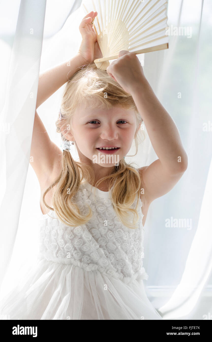 unschuldiges kleines Mädchen sitzen durch den Vorhang und weißen Lüfter über den Kopf halten Stockfoto