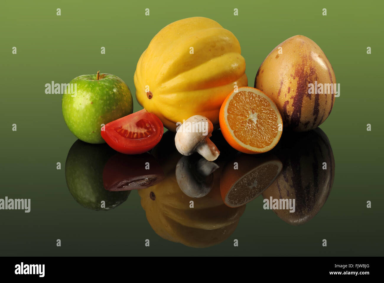 Frisches Obst und Gemüse auf reflektierenden Tisch auf grünem Hintergrund Stockfoto