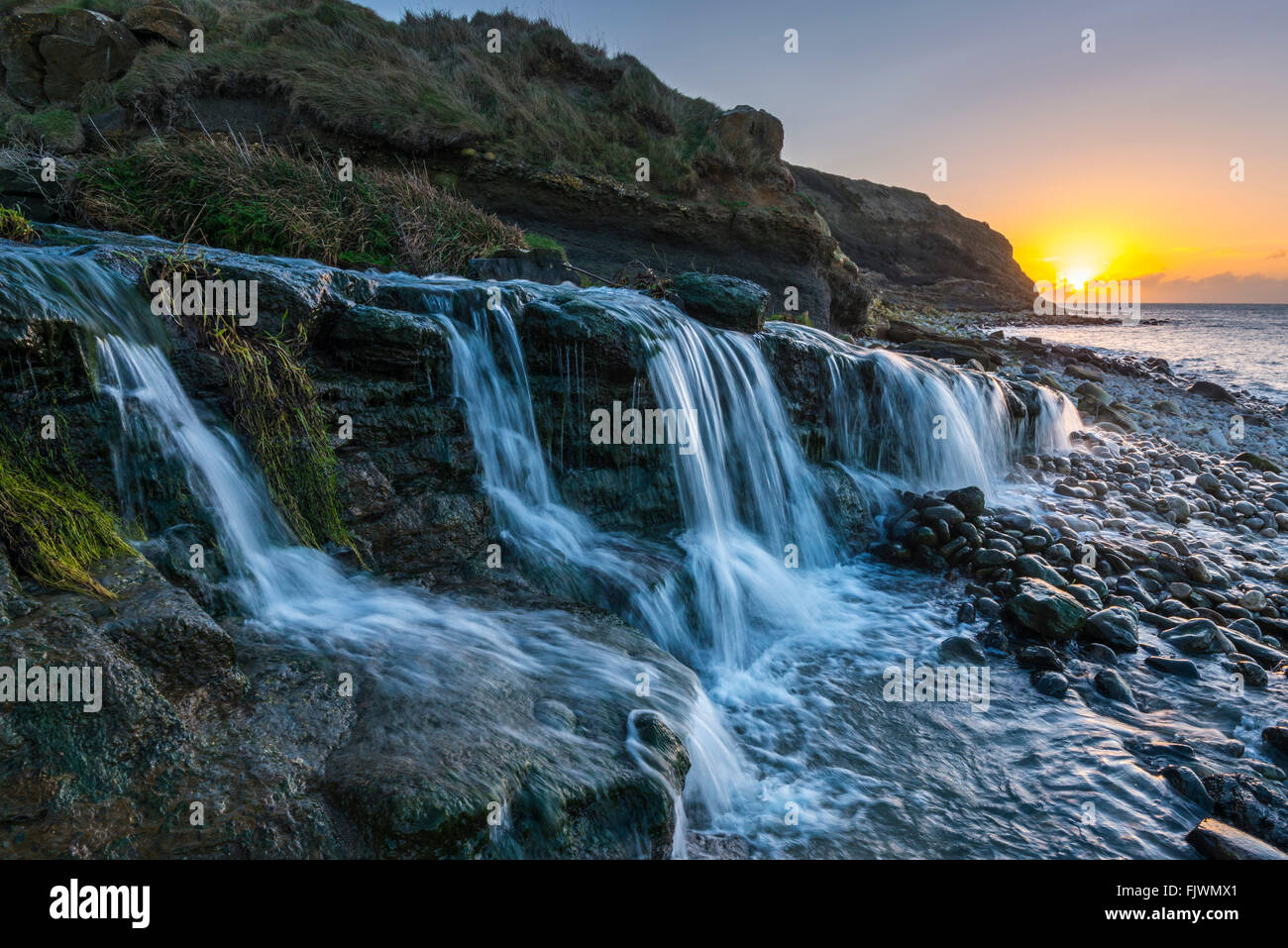 Bei Sonnenaufgang fließt ein Wasserfall zum Strand von Osmington Mills an der Jurassic Coast von Dorset. Bildnachweis: Graham Hunt/Alamy Stockfoto