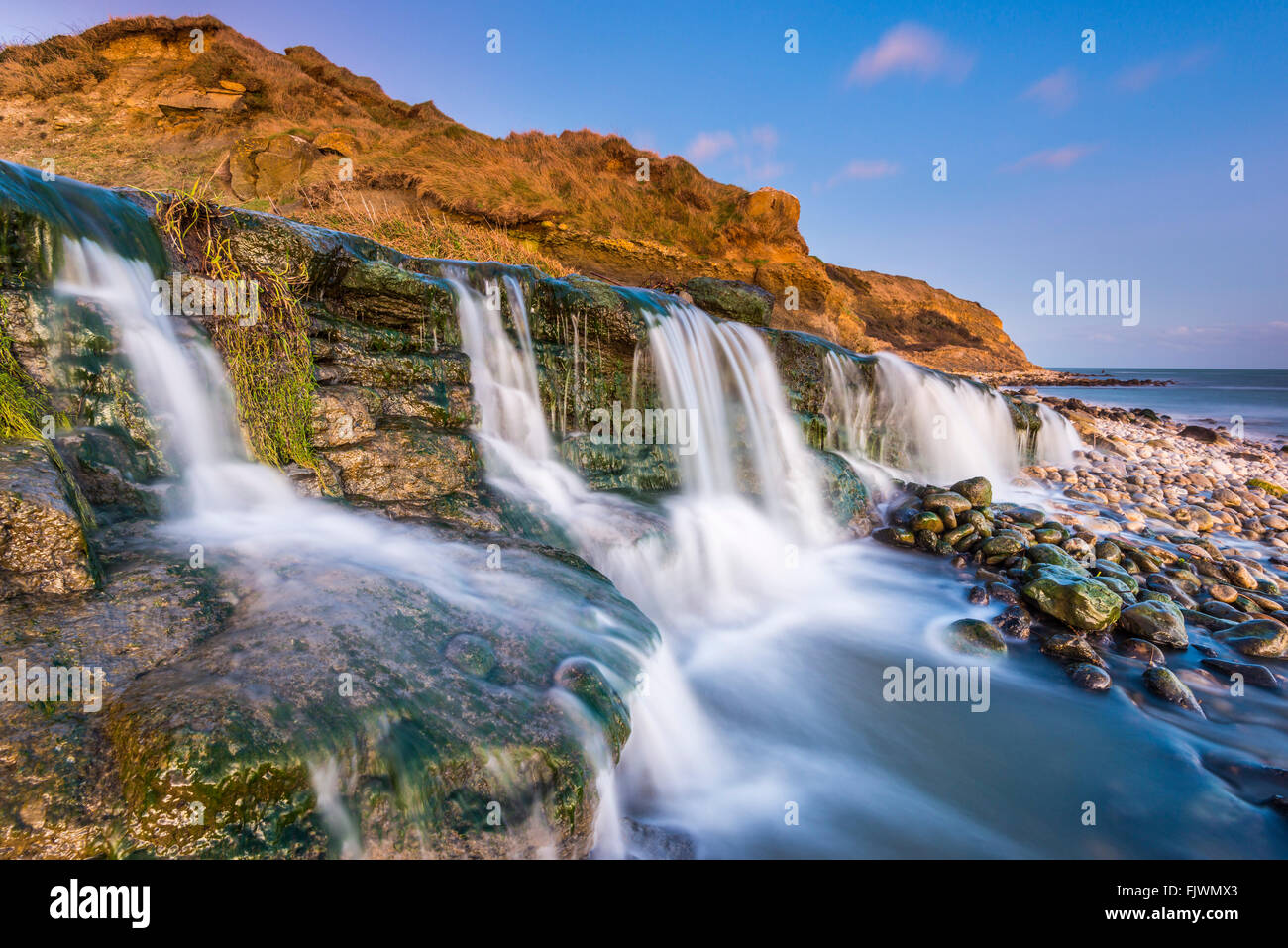 In der Abenddämmerung fließt ein Wasserfall zum Strand von Osmington Mills an der Jurassic Coast von Dorset. Bildnachweis: Graham Hunt/Alamy Stockfoto