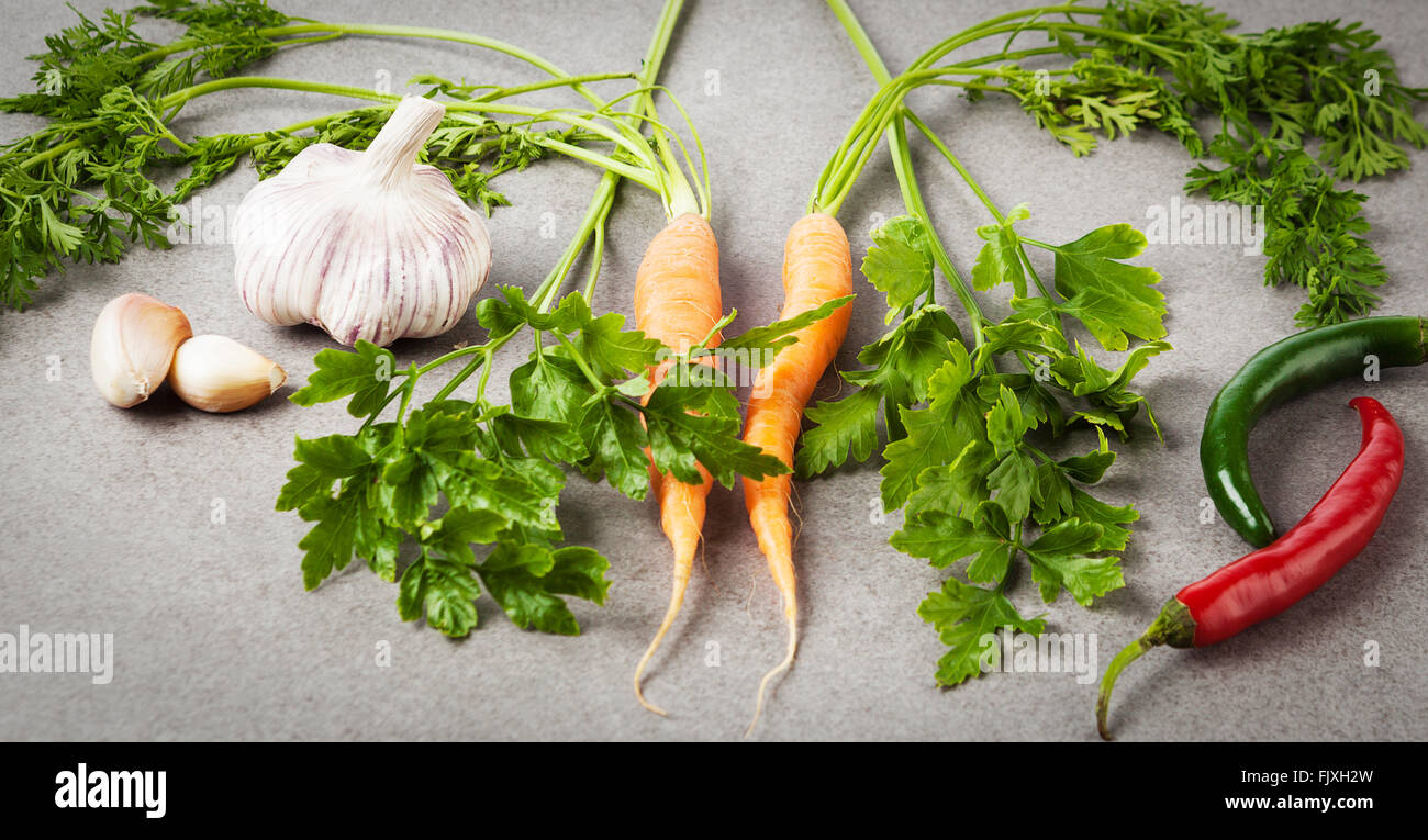 Niederländische Karotten, Petersilie, Knoblauch und hot chili Peppers auf strukturierten Stein Hintergrund. Rohkost-Zutaten. Stockfoto