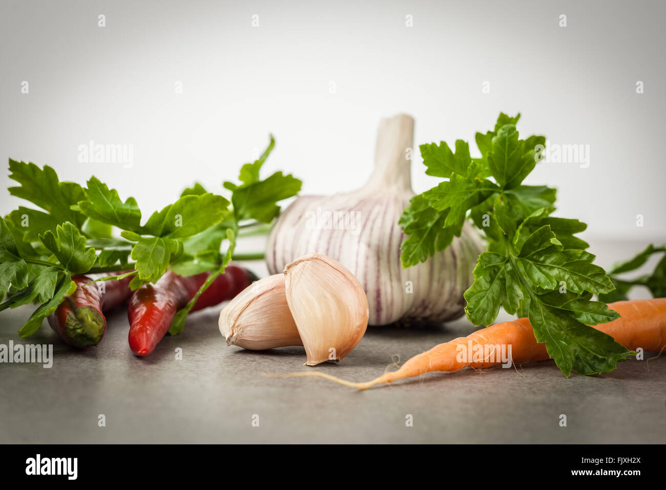 Niederländische Karotten, Petersilie, Knoblauch und hot chili Peppers auf strukturierten Stein Hintergrund. Rohkost-Zutaten. Stockfoto