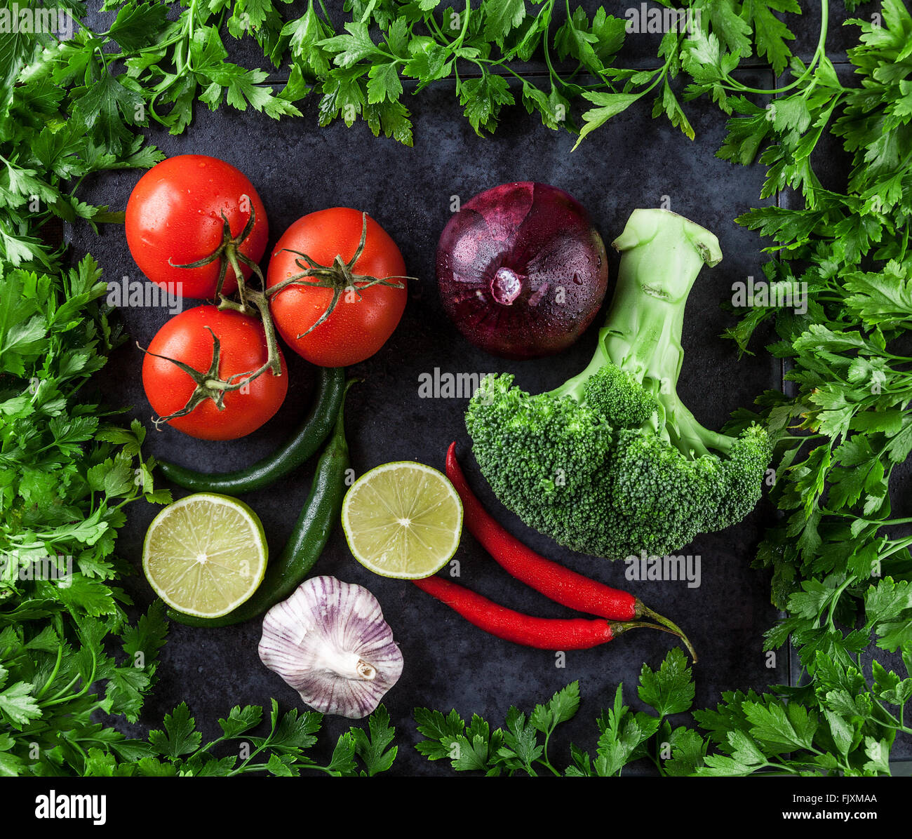 Tomaten, scharfe Chilischoten, Knoblauch, Zwiebel, Kalk und Brokkoli mit Petersilie auf Grunge Hintergrund umrahmt. Ansicht von oben. Stockfoto