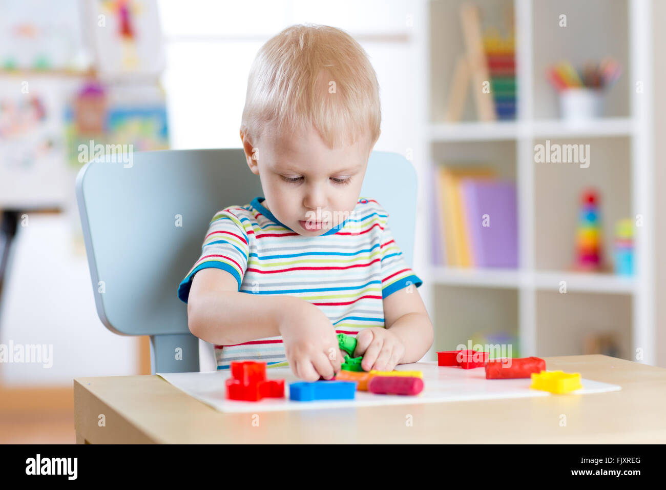 Kleiner Junge lernen, bunte Knete im Kinderzimmer zu nutzen Stockfoto