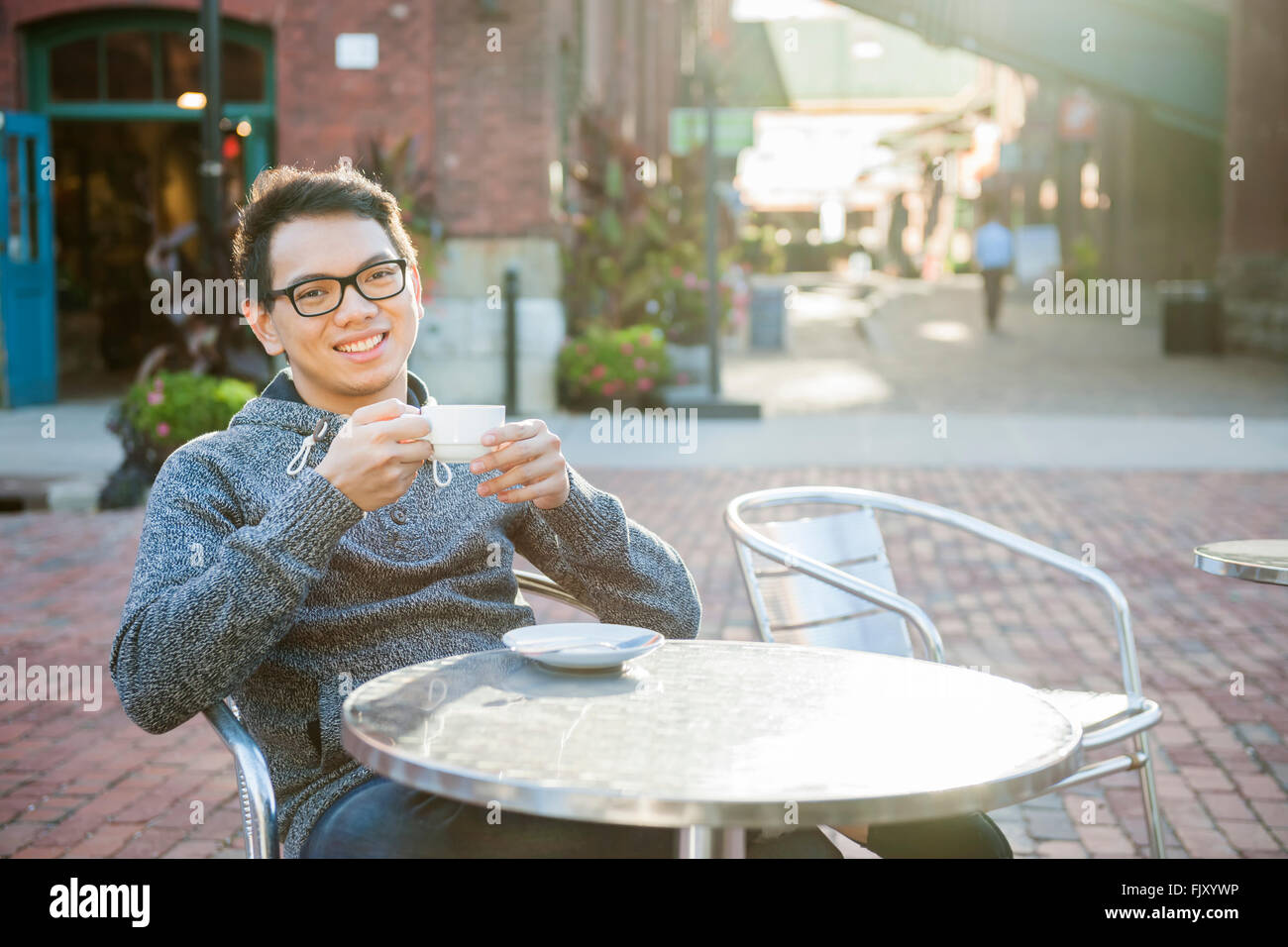 Junge asiatische Mann lächelnd in entspannende Freiluft-Café mit Kaffee Stockfoto