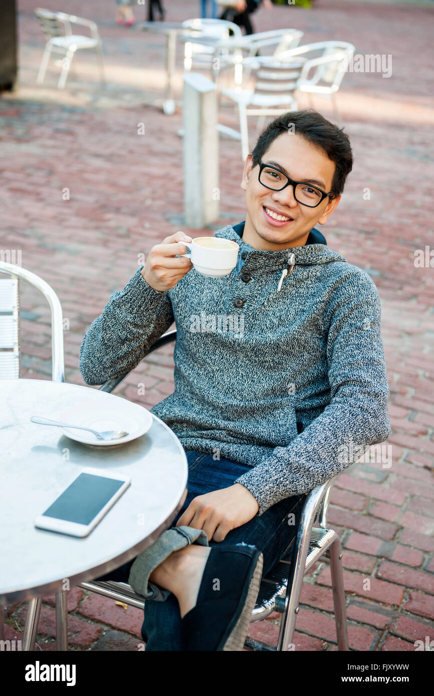 Junge asiatische Mann lächelnd in entspannten outdoor-Café mit Handy halten Tasse Kaffee Stockfoto