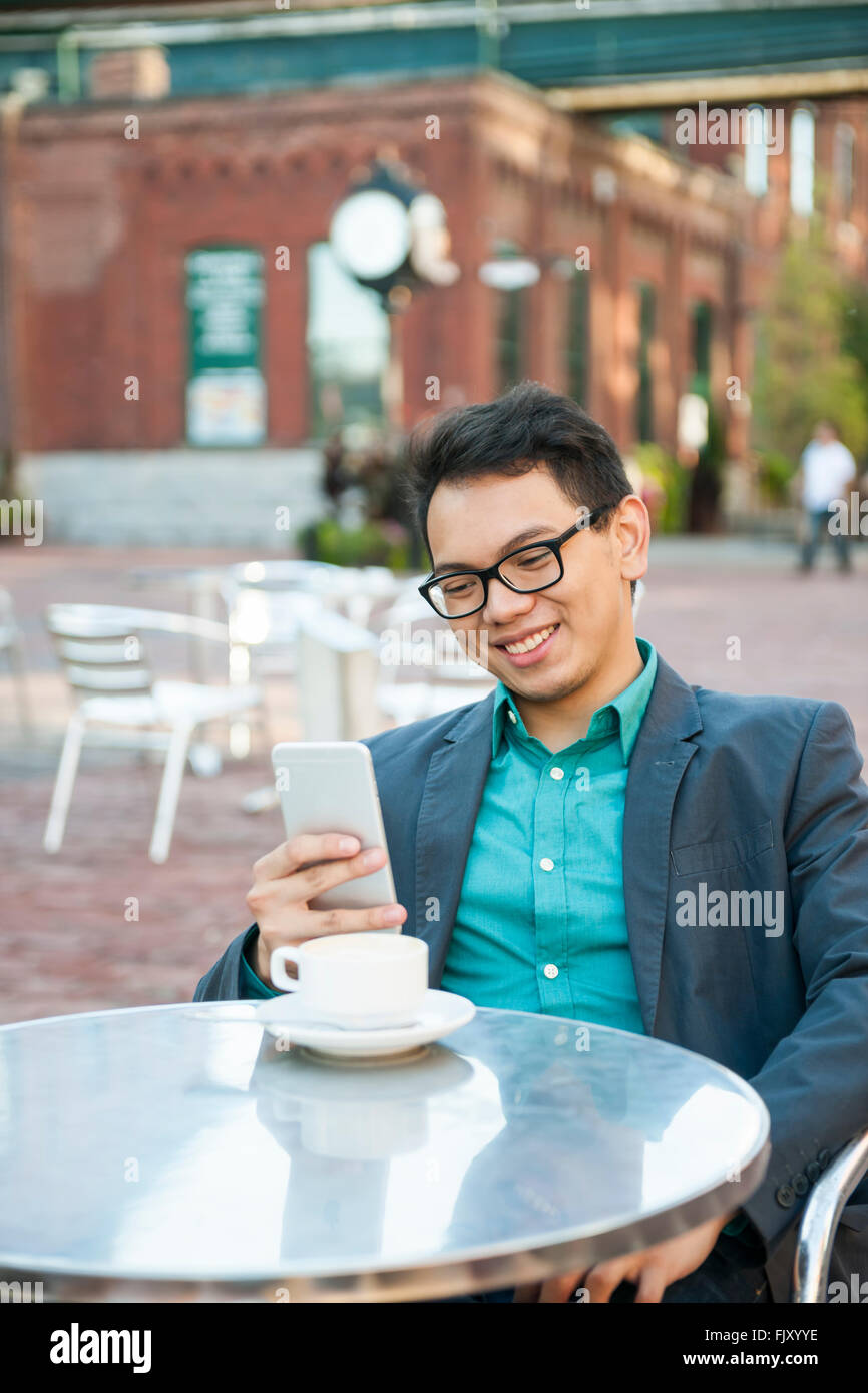 Erfolgreiche junge asiatische Mann in casual Geschäftskleidung lächelnd in entspannten outdoor-Café mit Tasse Kaffee mit Blick auf Stockfoto