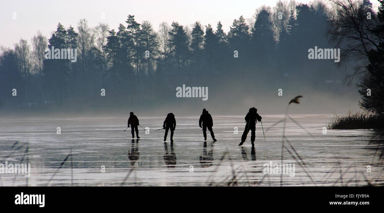 Vier silhuetts von Menschen lange gehen - Abstand Schlittschuhlaufen auf zugefrorenen See Stockfoto