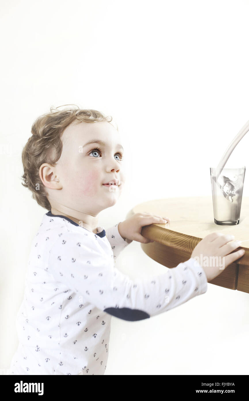 kleiner Junge durch den Holztisch mit Glas Milch Stockfoto