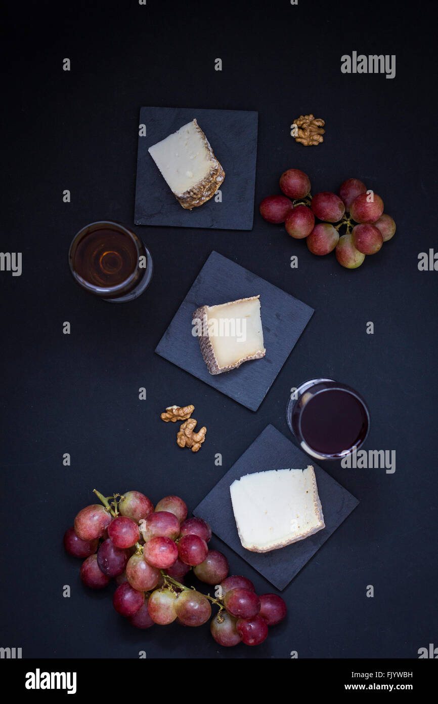 Käsestücke auf schwarzem Hintergrund, begleitet von Wein, Sherry und Walnüssen Stockfoto