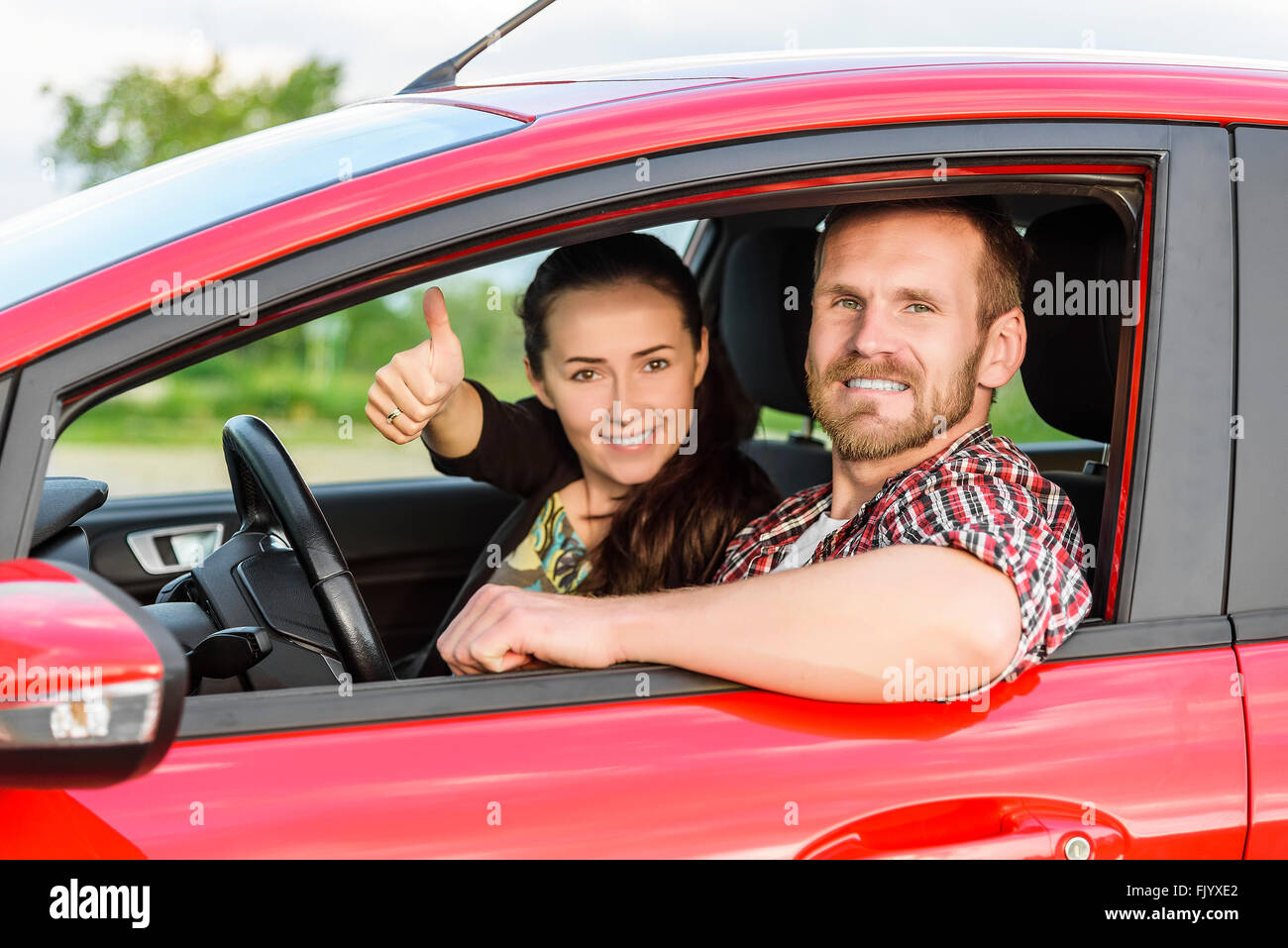Zwei junge, lächelnde Menschen in einem roten Auto Stockfoto