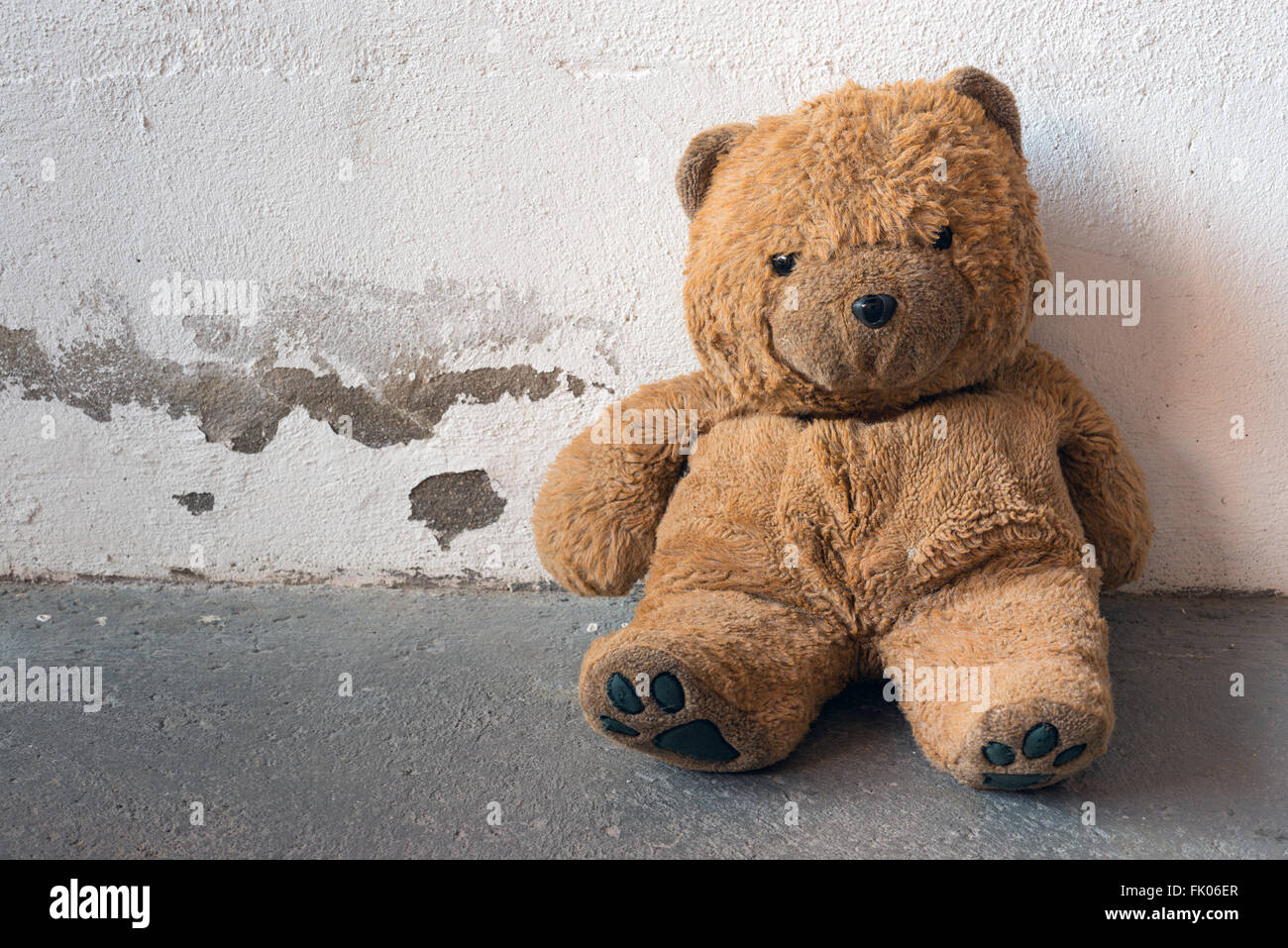 Ein alt und schmutzig Teddybär ist gegen eine weiße Betonwand sitzen. Stockfoto