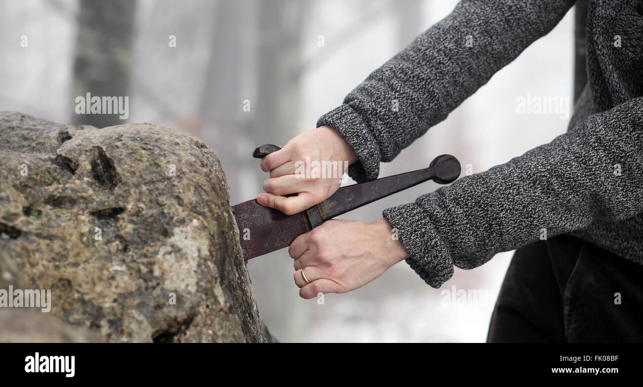 Hand des tapferen Ritters versucht, das magische Schwert Excalibur in den Stein zu entfernen Stockfoto