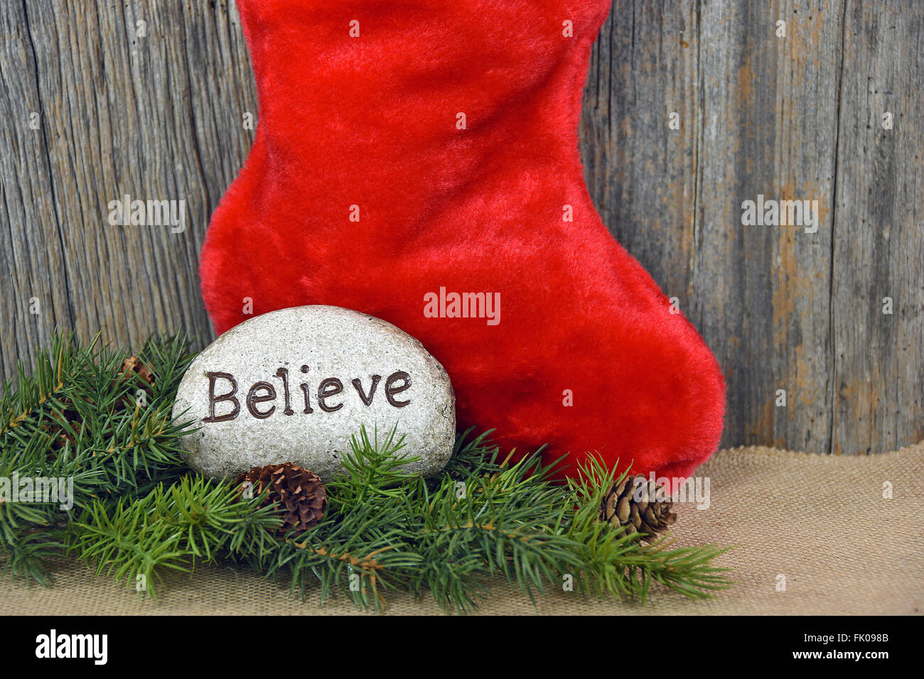 Wort "glauben", gedruckt auf einem Felsen mit grünen Ast und rote Weihnachts-Strumpf. Stockfoto