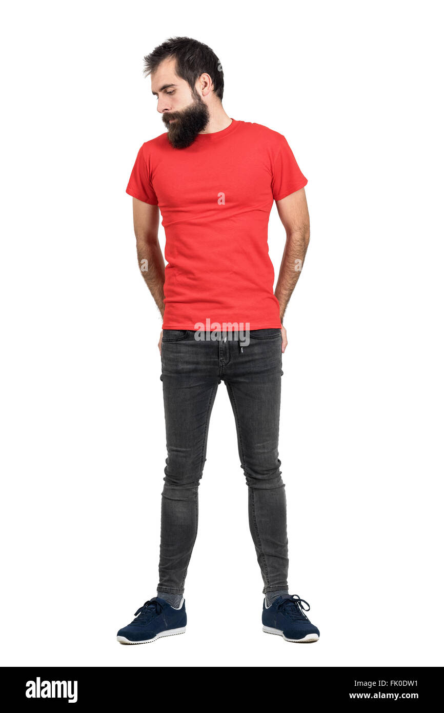 Ernsthafte bärtige Hipster im roten T-shirt mit Händen in seine Gesäßtasche blickte. Ganzkörper-Länge-Porträt über weißen isoliert Stockfoto