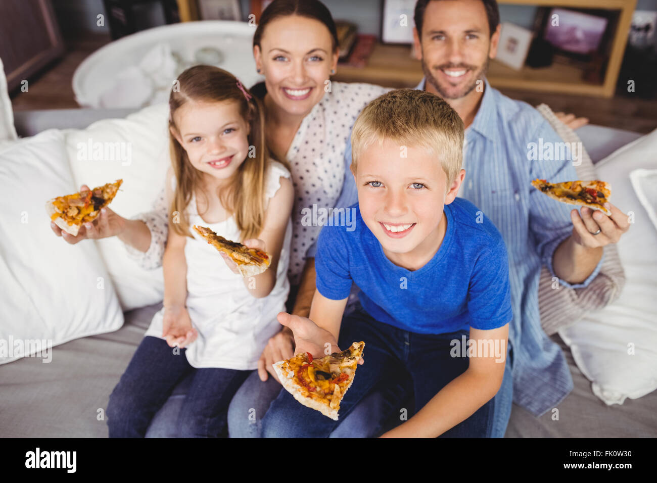 Porträt des Lächelns Familienholding Pizza Scheiben sitzend auf sofa Stockfoto