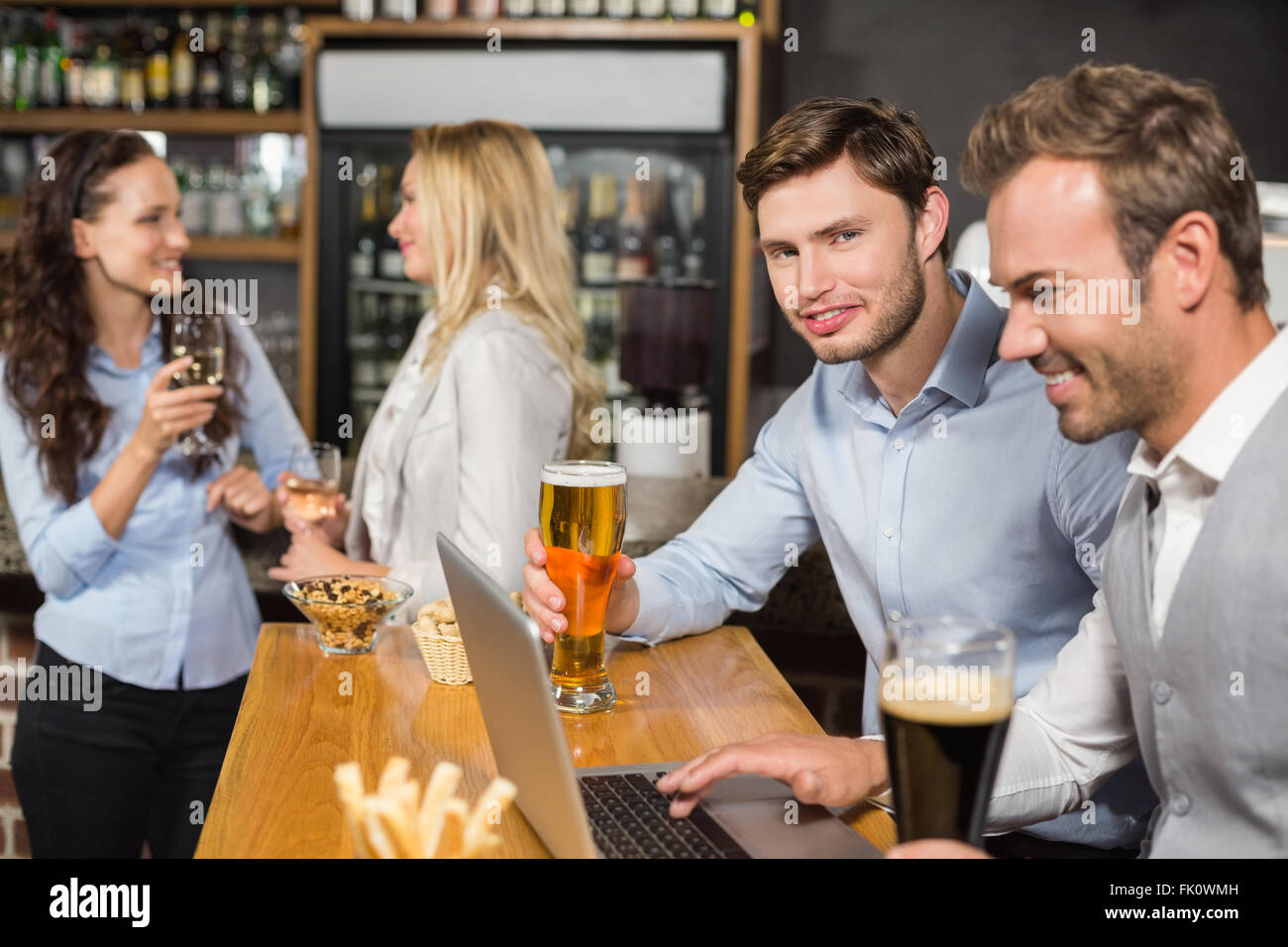 Männer arbeiten am Laptop, während Frauen hinter reden Stockfoto