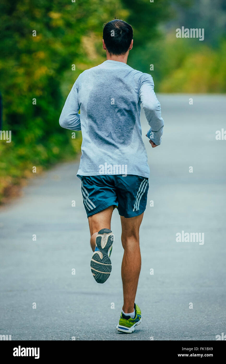 männlicher Athlet läuft im Park eine asphaltierte Straße. Blick vom Rücken in ein Sweat-shirt Stockfoto