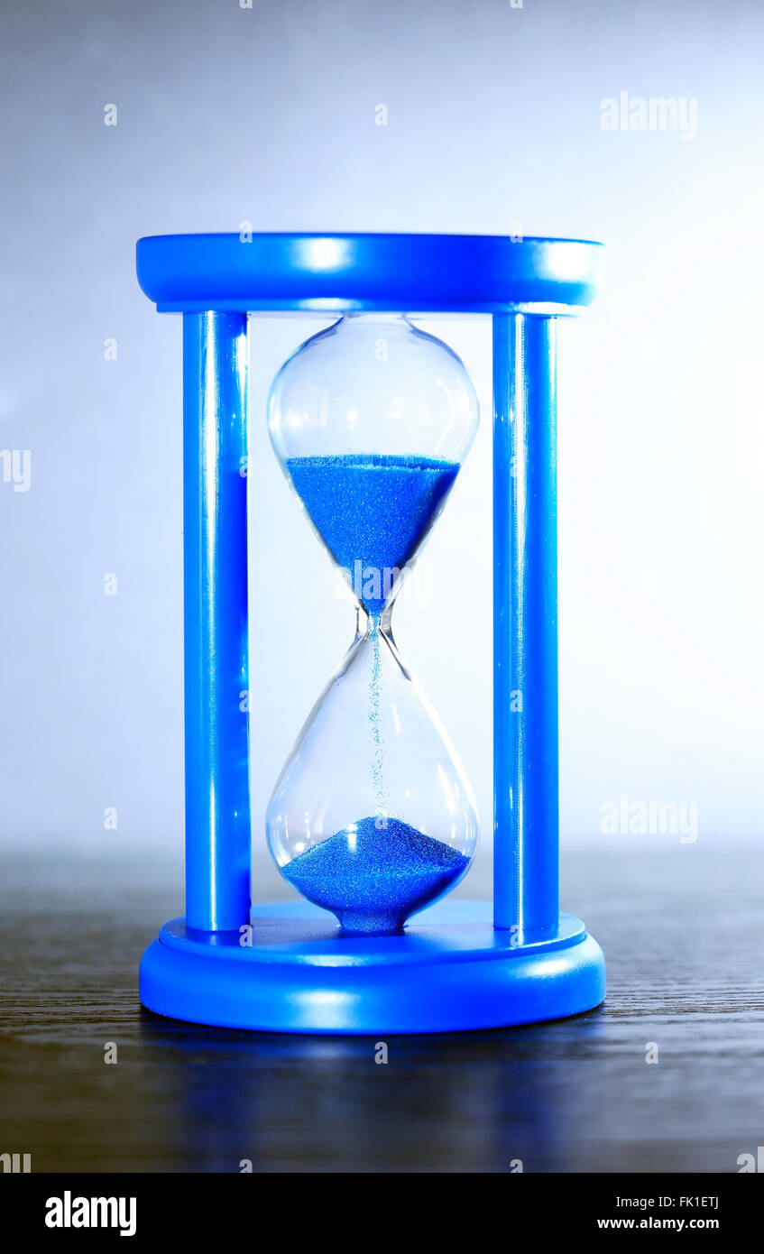 Zeit-Konzept. Sanduhr mit blauem Sand am schönen grauen Hintergrund Stockfoto