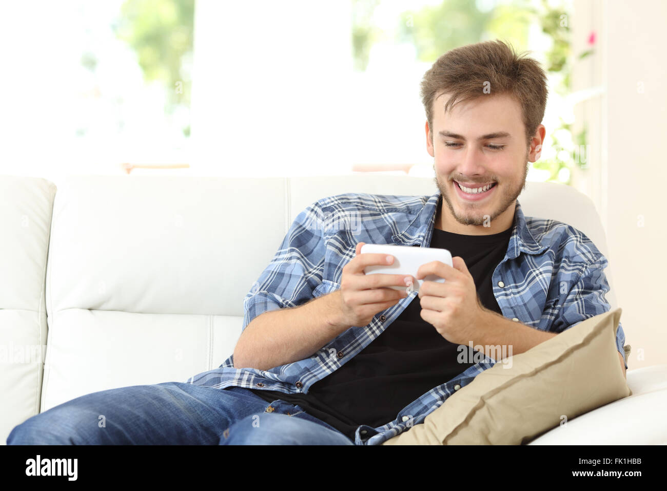 Mann mit einem Smartphone sitzen auf einer Couch zu Hause Online-Spiele spielen Stockfoto