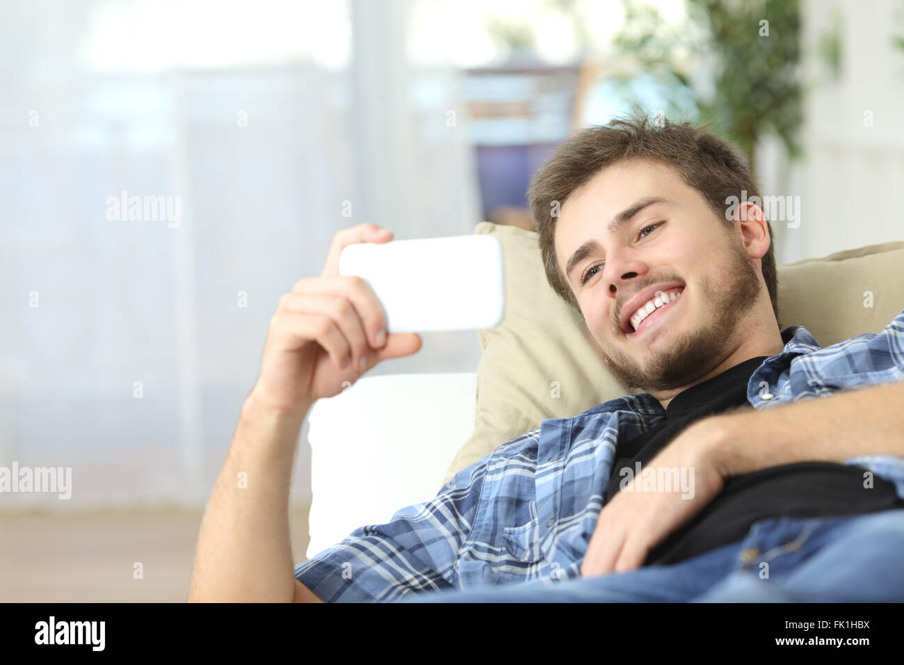 Glücklicher Mann Filme in ein smart Phone auf einer Couch zu Hause Stockfoto