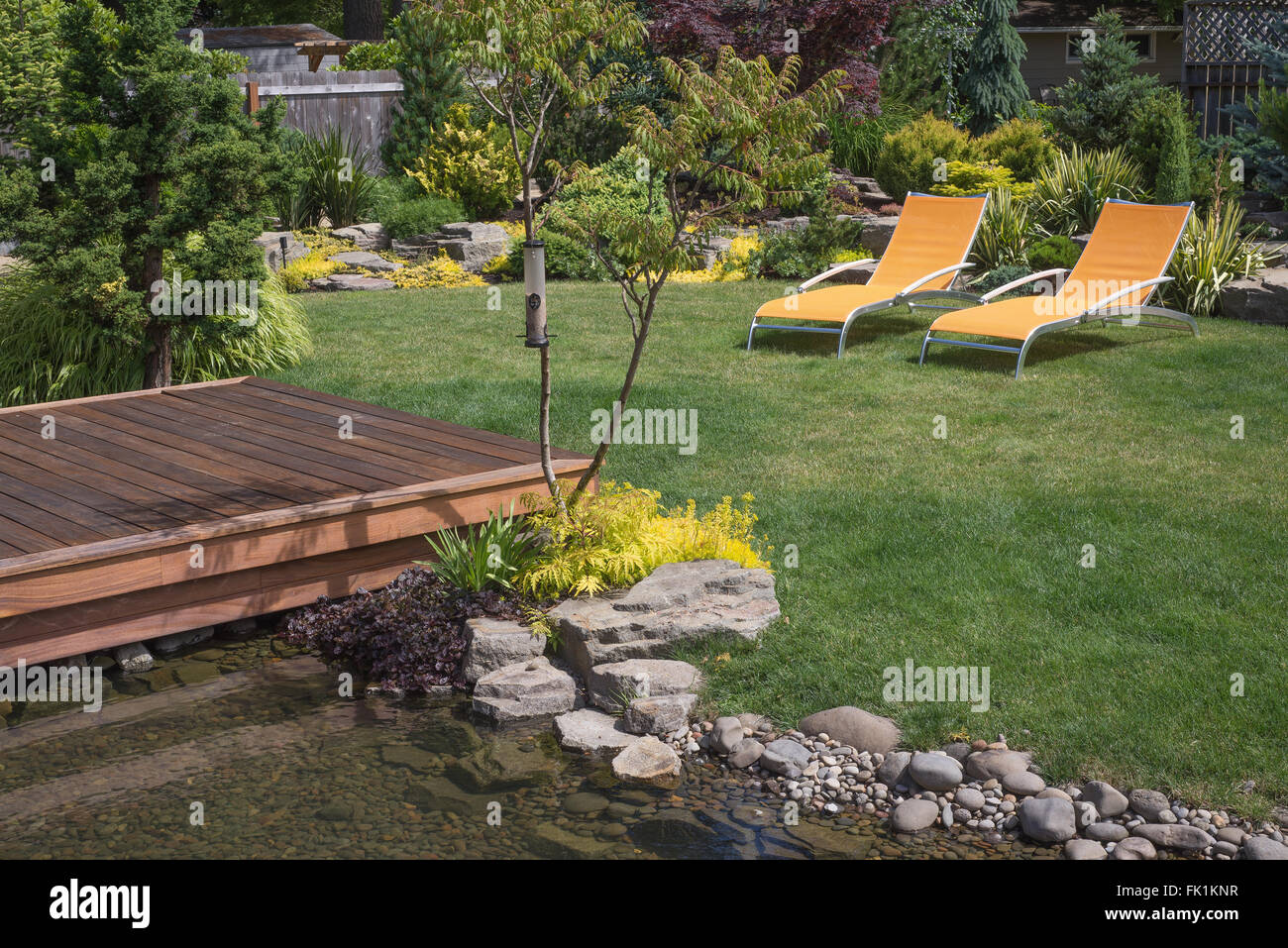 Ein paar helle gelbe Designer Liegestühlen lädt zum Entspannen in diesem wunderschön angelegten Garten mit überspannt eine Cr-deck Stockfoto