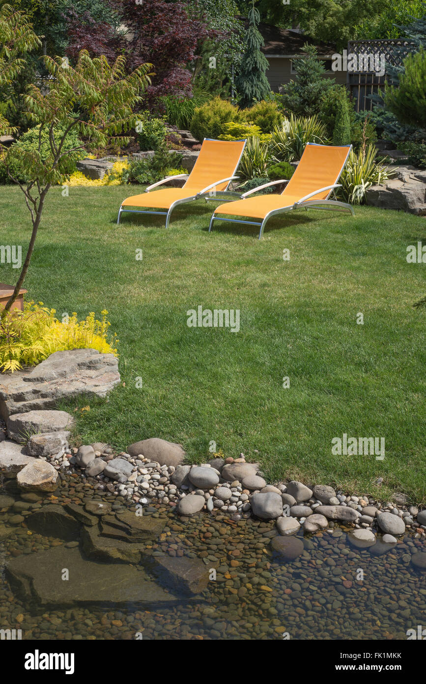 Ein paar helle gelbe Designer Liegestühlen lädt zum Entspannen in dieser wunderschön angelegten Garten mit einer Stein-gefüllte cre Stockfoto
