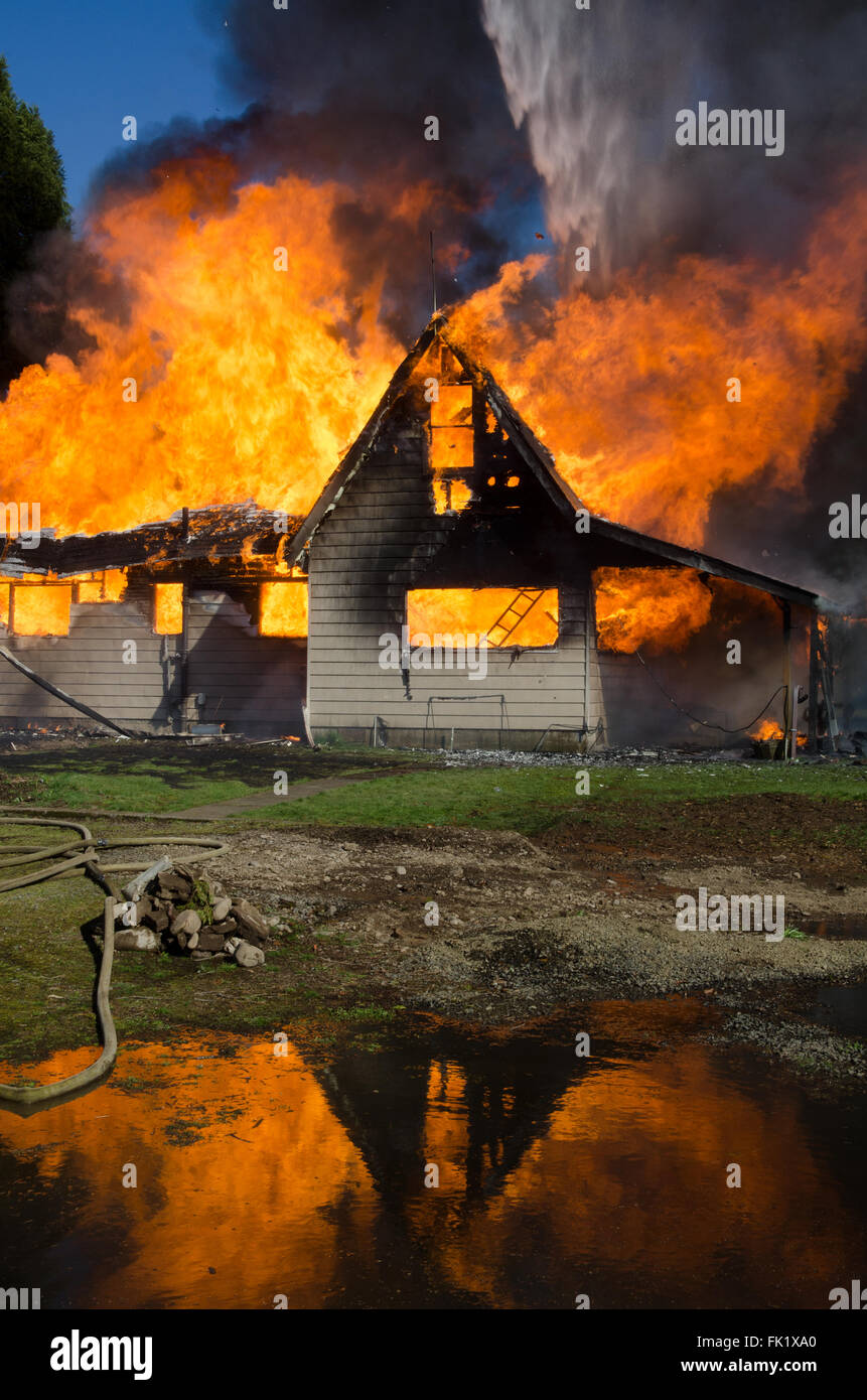 Der Flammen eines brennenden Hauses spiegelt sich in einem Pool des Abflusses aus Feuerwehrschläuchen. Stockfoto