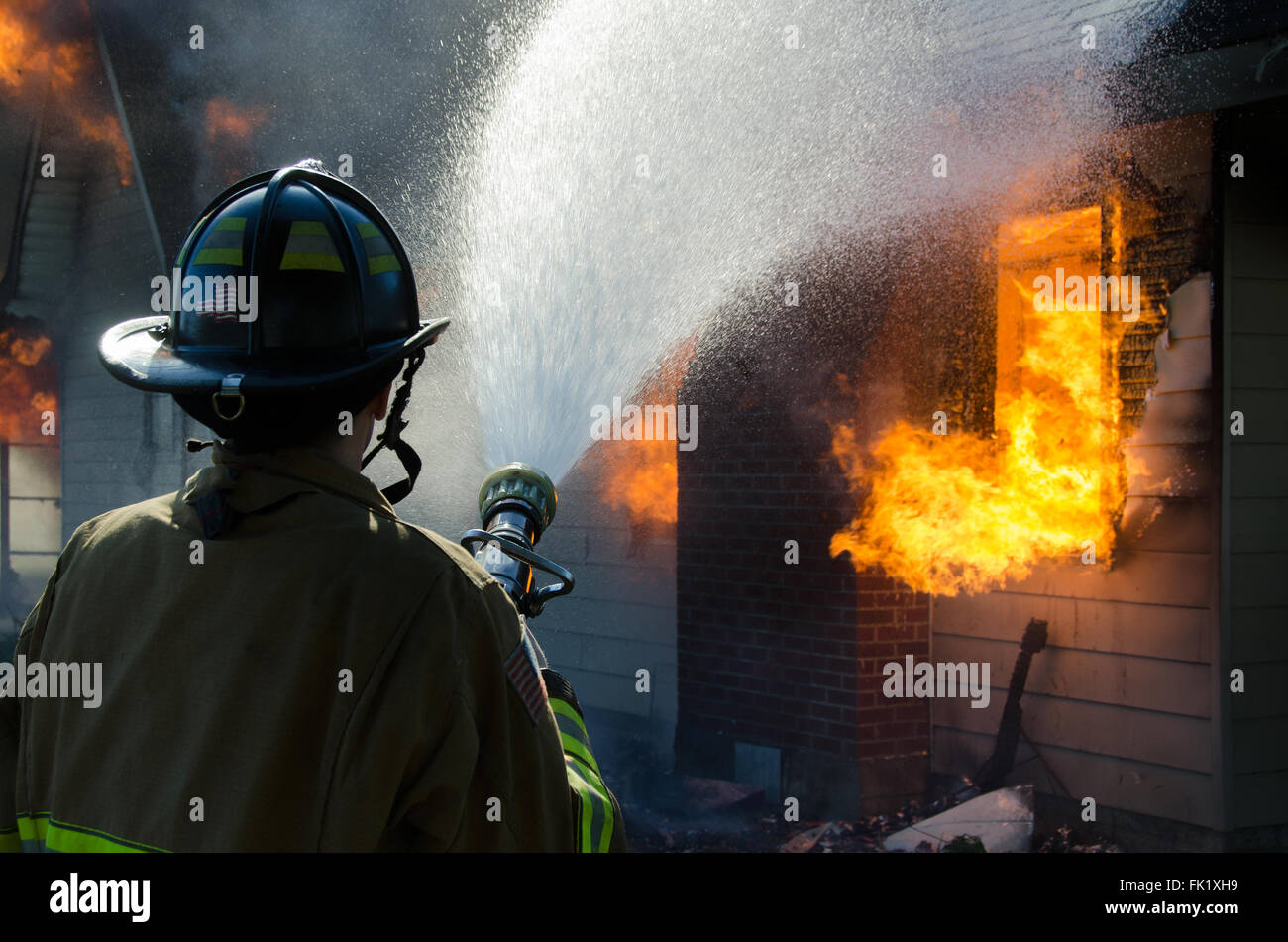 Ein Feuerwehrmann ergießt sich einen Strom von Wasser auf einem brennenden Haus. Stockfoto