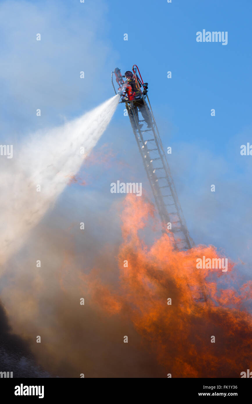 Ein Feuerwehrmann strömt eine Explosion von Wasser von einem Ariel Pumpe Leiter hoch über eine Feuersbrunst. Stockfoto