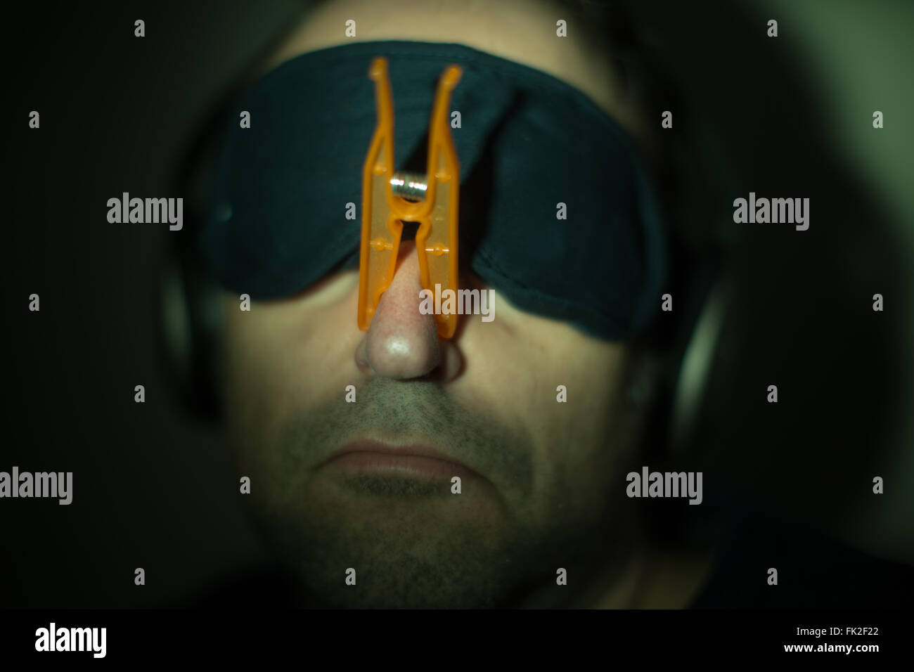Ein Mann trägt eine Wäscheklammer auf der Nase, Kopfhörer und eine Augenmaske Stockfoto