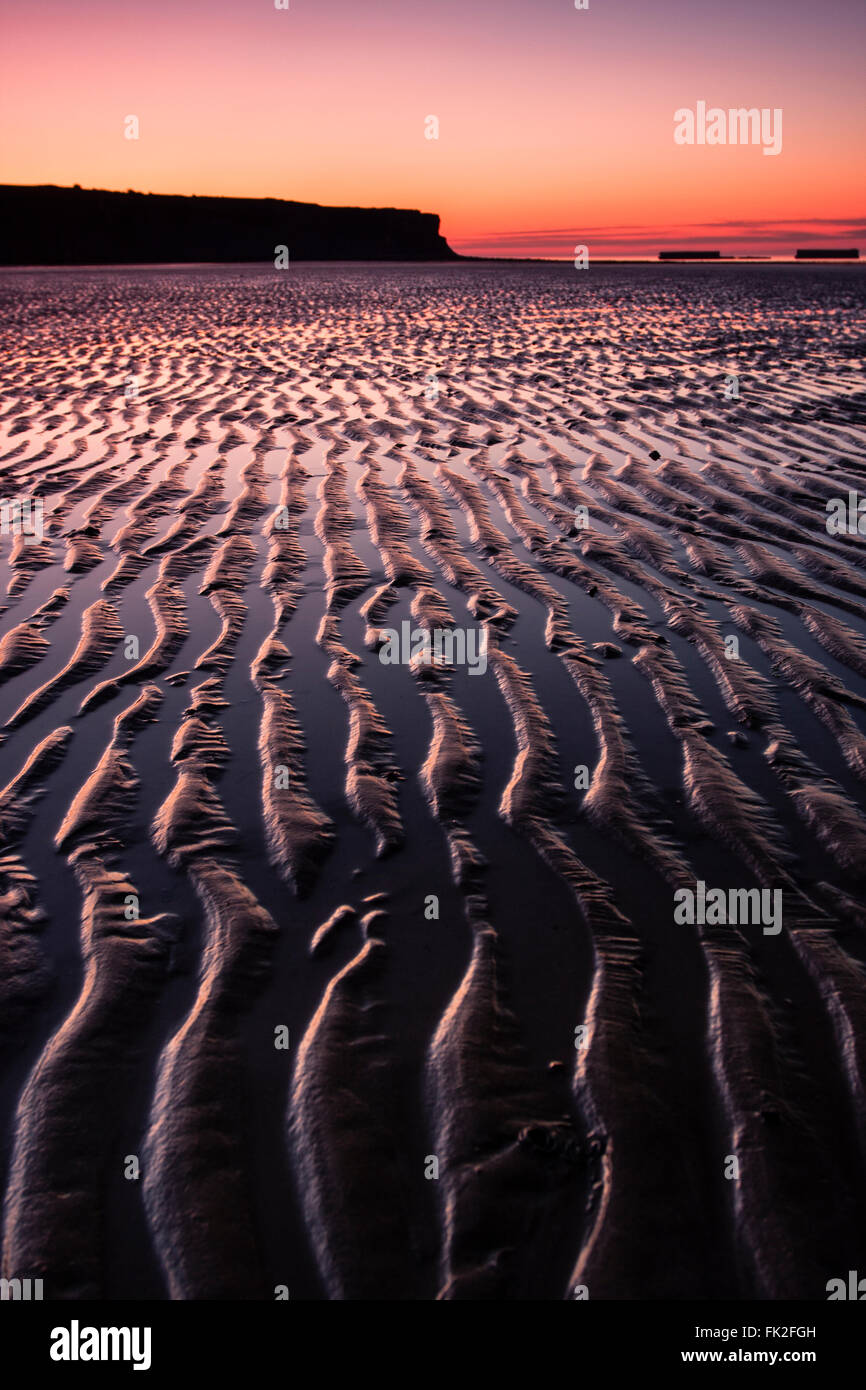 Am Strand von Arromanches-Les-Bains, Normandie, erhöht das Licht der Morgendämmerung die Linien im nassen Sand. Stockfoto