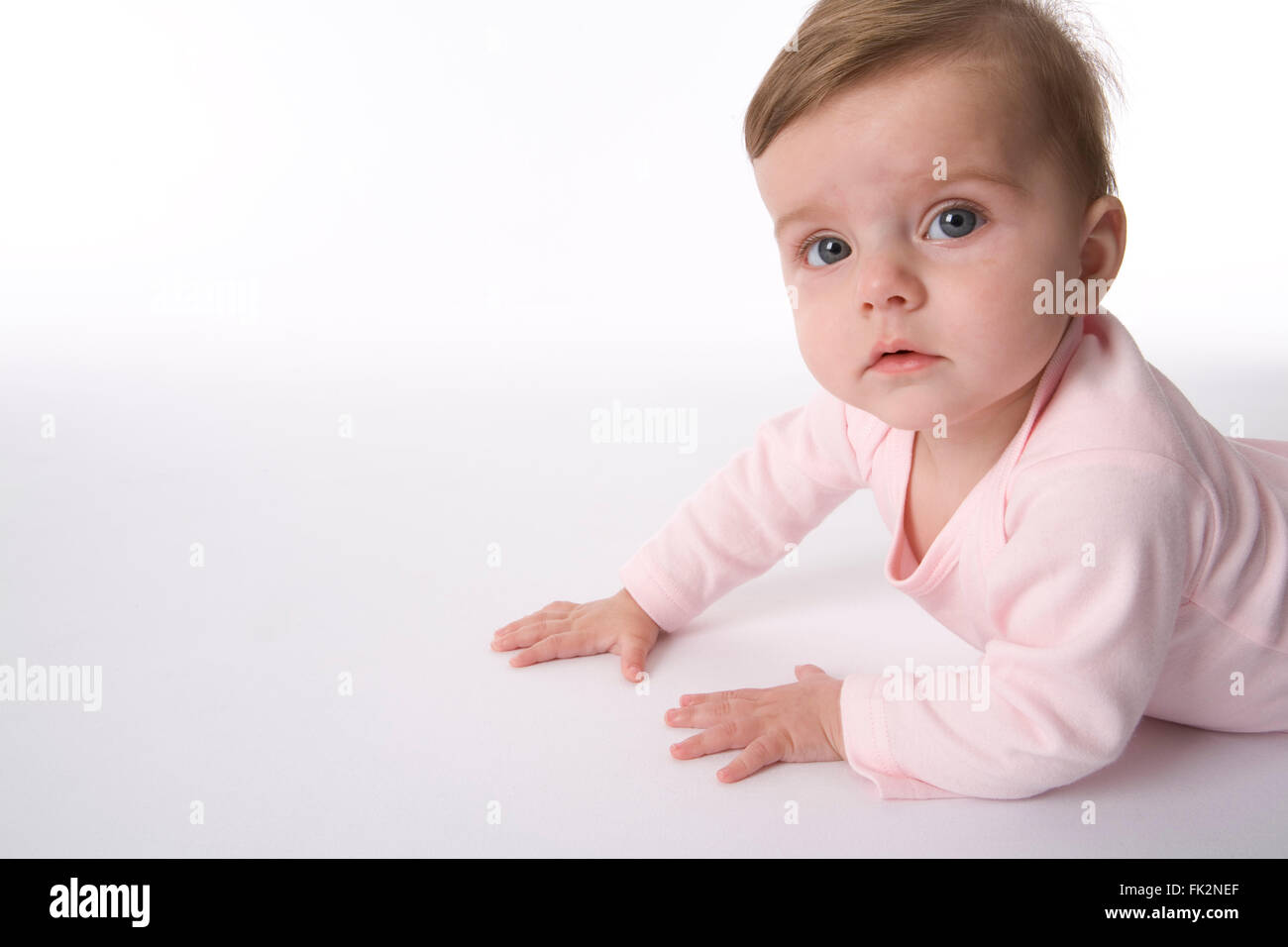 Baby Mädchen ist liegend auf ihr Bauch auf der Suche in der Kamera auf weißem Hintergrund Stockfoto