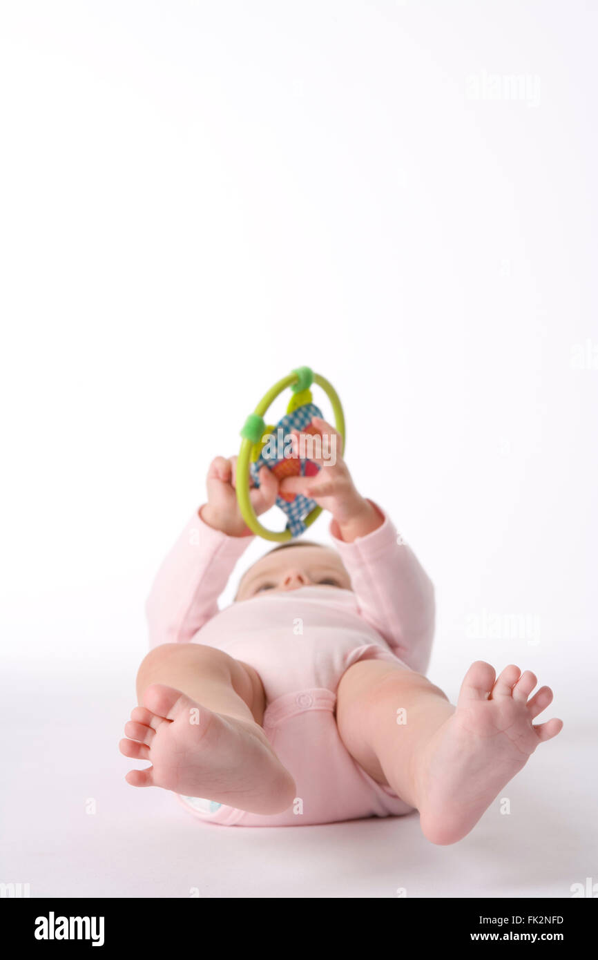 Baby Mädchen liegen auf dem Boden spielen mit A Toy auf weißem Hintergrund Stockfoto