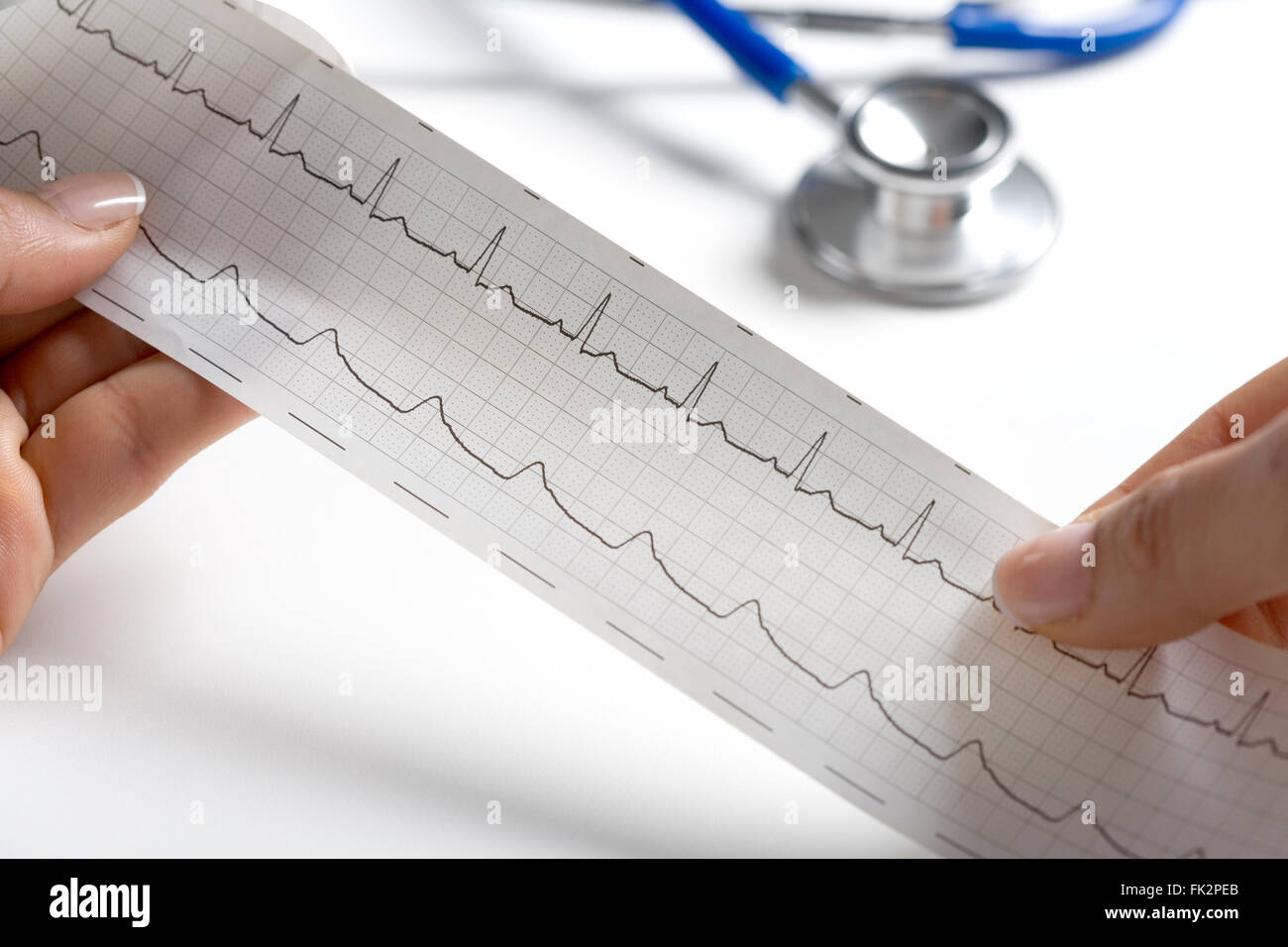Hände halten eine regelmäßige EKG mit einem Stethoskop im Hintergrund Stockfoto