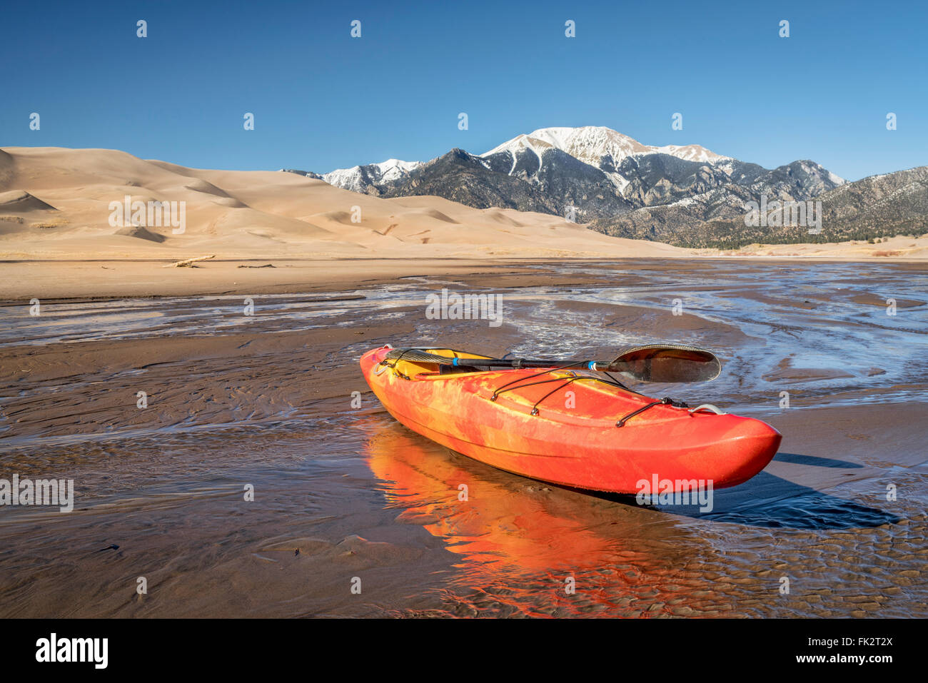 Wildwasser-Kajak in flachen Gewässern von Medano Creek mit Great Sand Dunes und Sangre De Cristo Mountains im Hintergrund Stockfoto