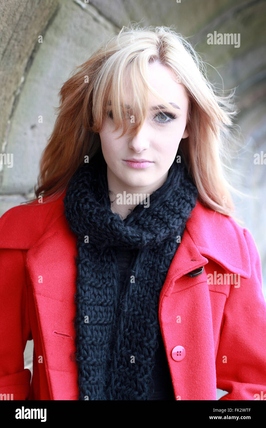 Schöne junge Frau mit blonden Haaren tragen rote Jacke und schwarze Schal an einem kalten, windigen Tag Stockfoto