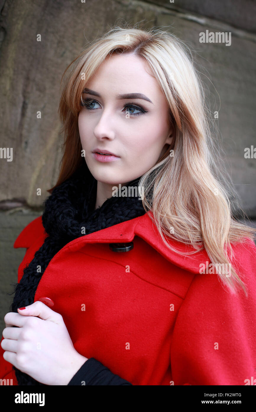 Schöne junge Frau mit blonden Haaren tragen rote Jacke und schwarze Schal an einem kalten, windigen Tag Stockfoto
