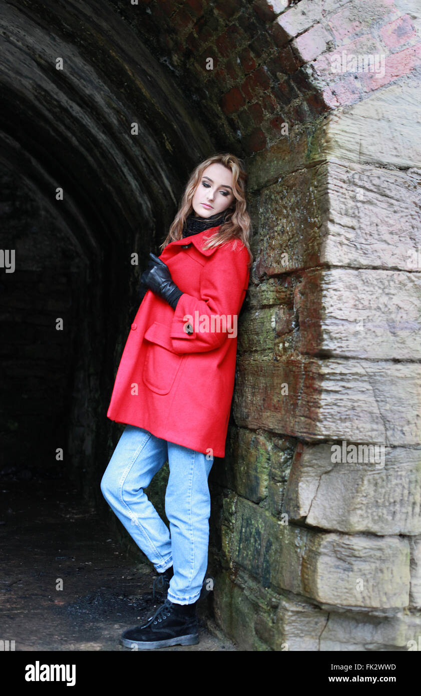 Frau trägt einen roten Mantel gelehnt eine alte Wand eines Tunnels Stockfoto