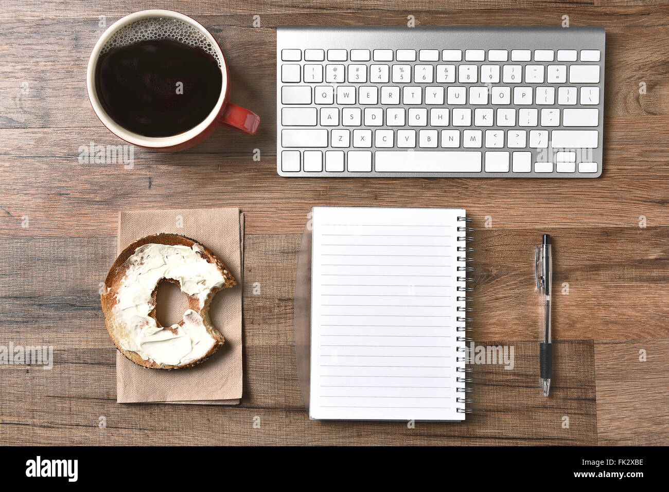 Ein Bagel mit Frischkäse und einen Imbiss neben einer Computer-Tastatur und einen Block und Stift herausgenommen. Stockfoto