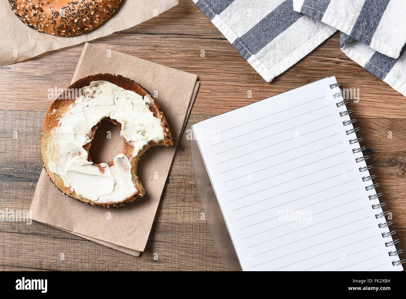 Ein Bagel mit Frischkäse und einen Imbiss neben einem Notizblock herausgenommen. Ansicht von oben im Querformat. Stockfoto