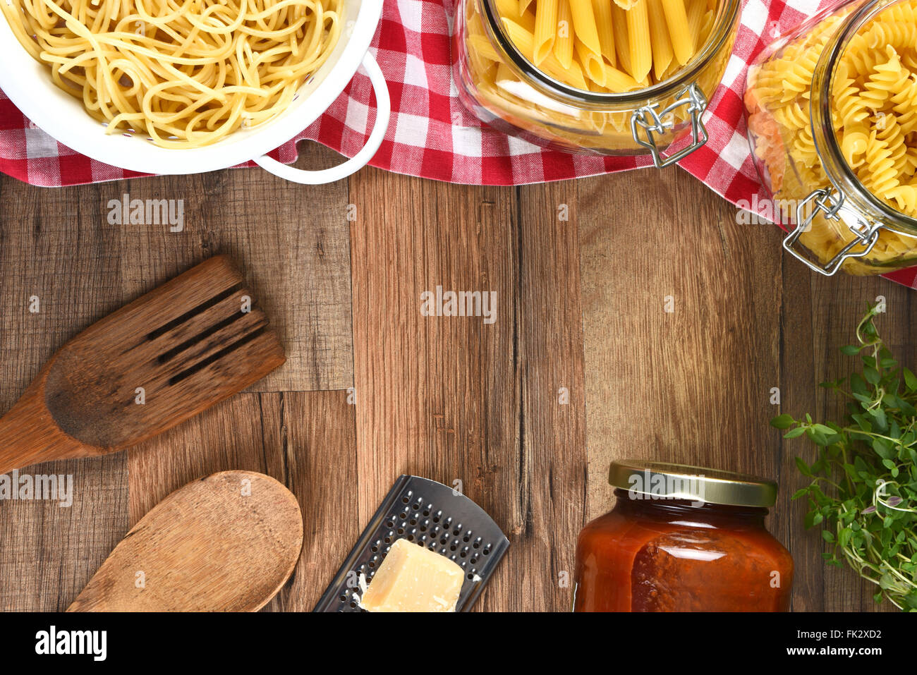 Vogelperspektive Blick auf eine Auswahl an Pasta, Parmesan, Käse, Reibe, Glas mit Sauce, Utensilien und Kräutern auf einer Holz Küche Tisch wi Stockfoto