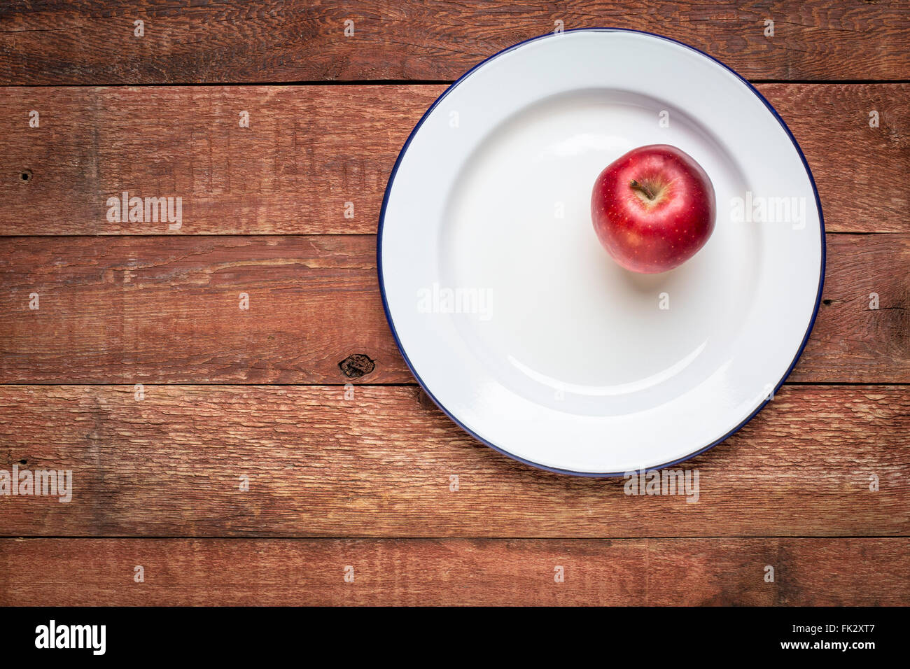 roter Apfel auf einem weißen Metall Emaille Teller gegen rustikale Holz - Essen Sie einen Apfel ein Tag-Konzept Stockfoto