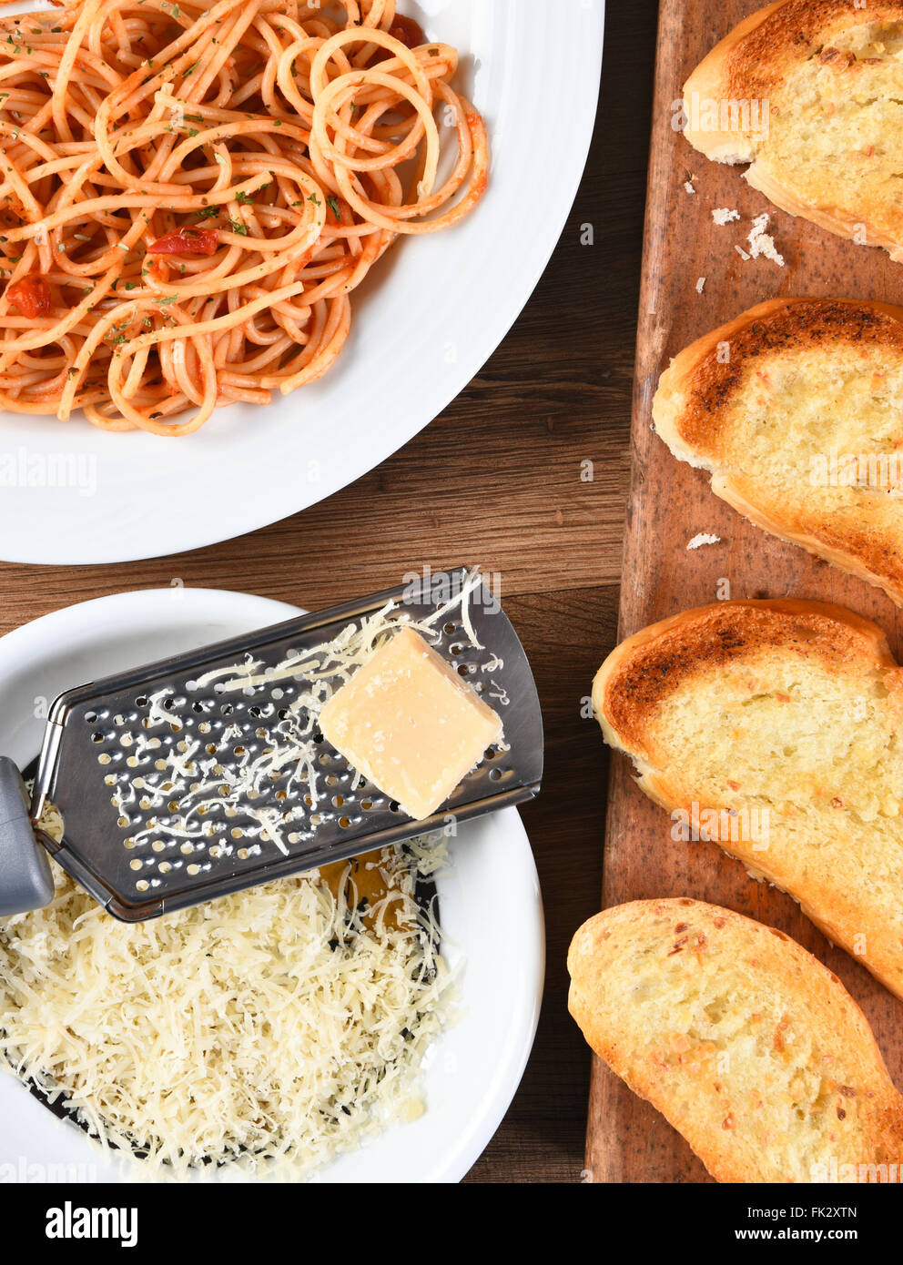 Draufsicht auf eine Käsereibe mit Parmesan-Käse auf einem rustikalen Holz Küchentisch. Einen Teller mit Spaghetti und Knoblauch Brot auf b Stockfoto