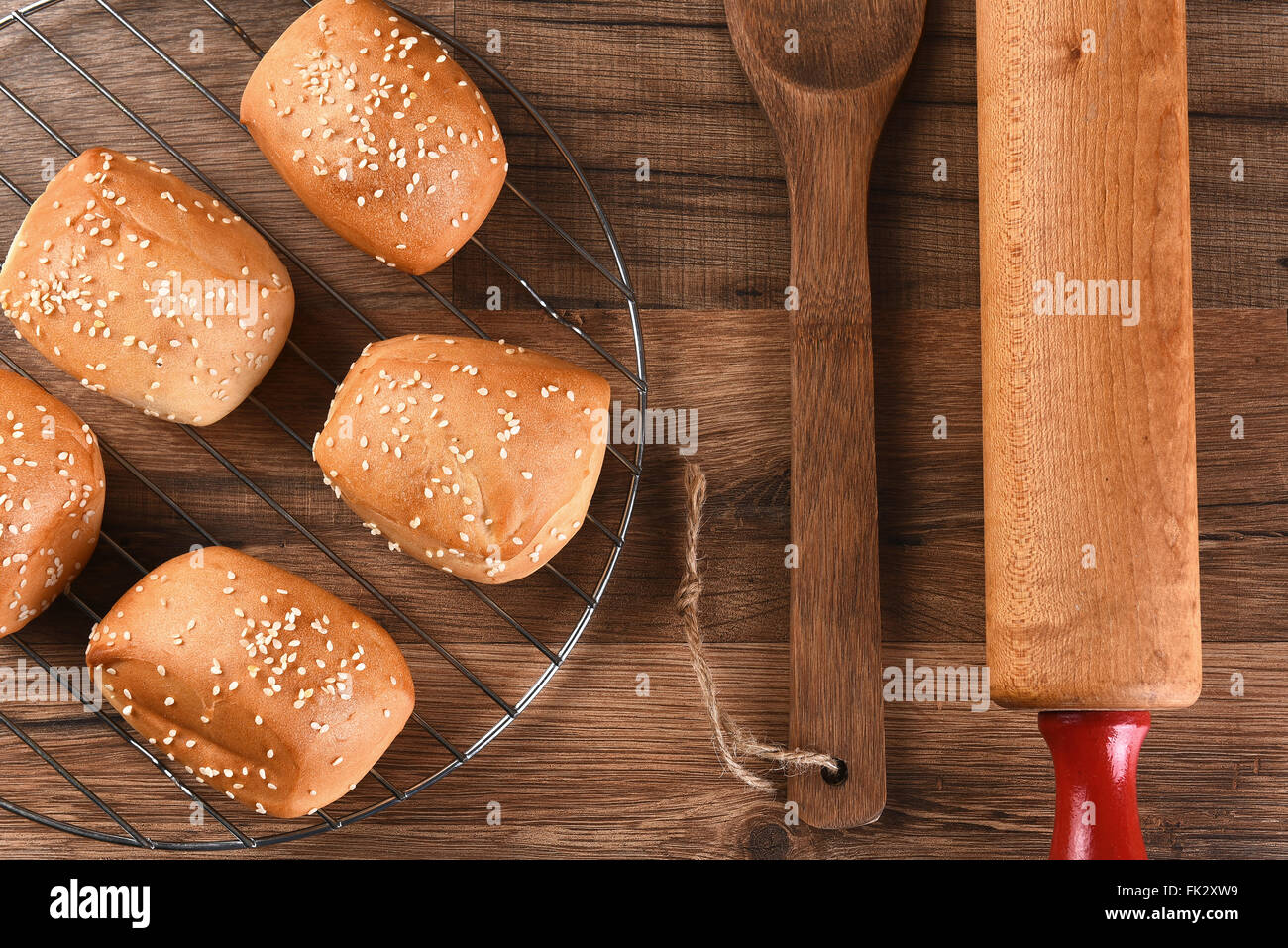 Draufsicht auf ein Rack mit Sesam Samen Abendessen Rollen neben einem Holzspatel und Nudelholz. Stockfoto
